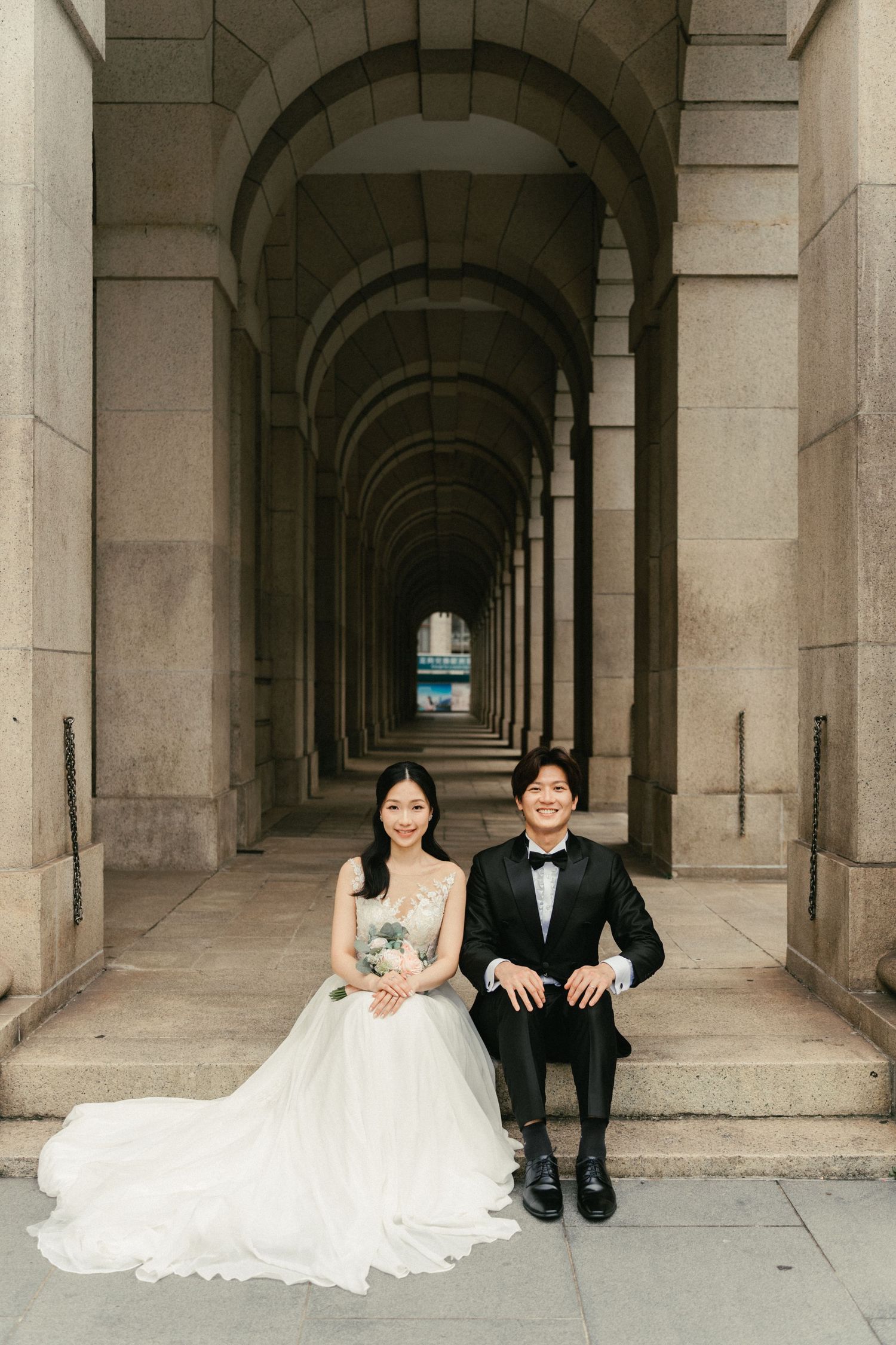 Bride and groom sitting together in a stunning arched stone corridor for a classic wedding portrait.
