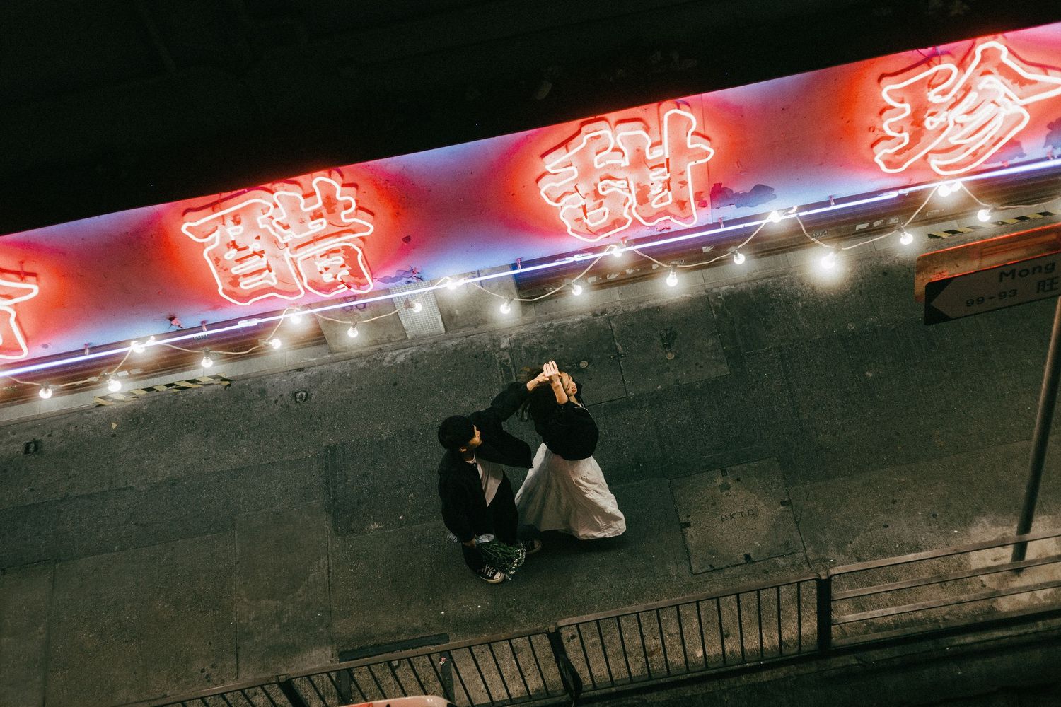 Aerial view of a couple embracing beneath glowing red Chinese neon signs at night.