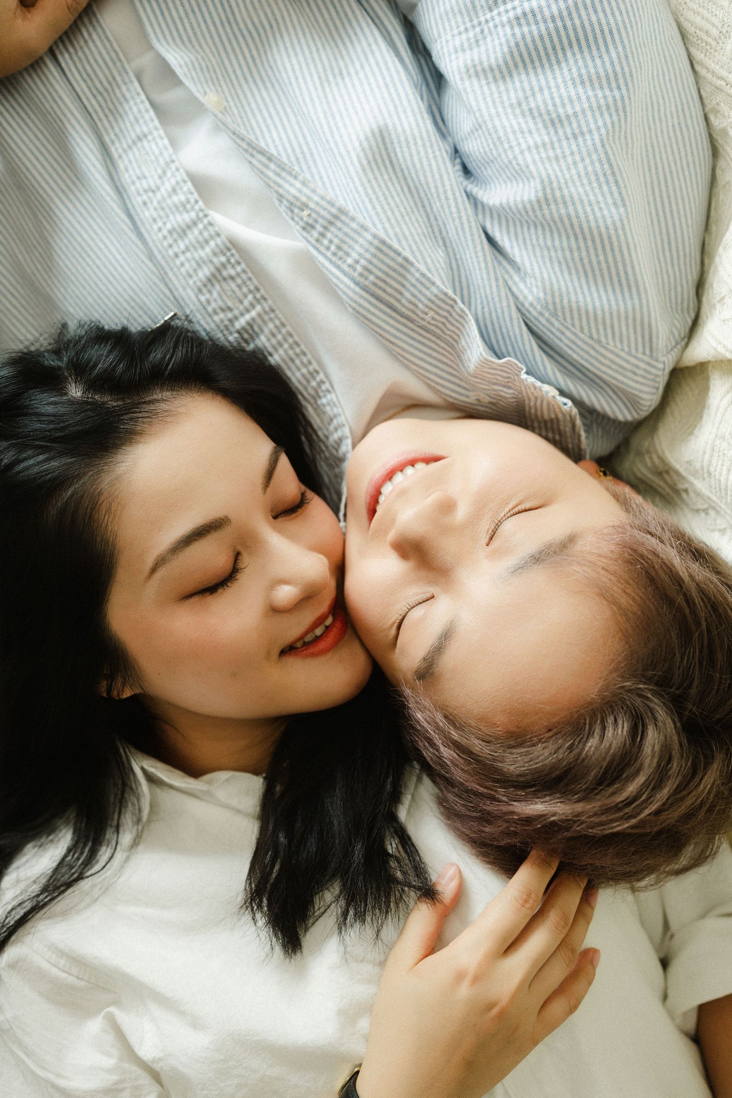 Couple lying down together smiling, woman resting her head close to partners face on white bedding.