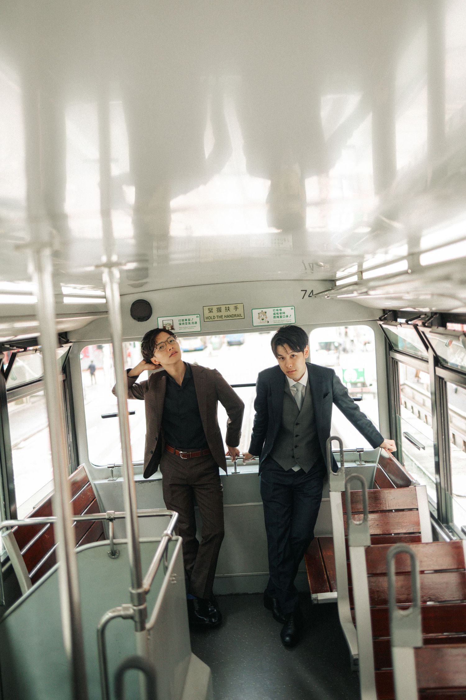 Two suited Asian men stand inside an empty vintage tram, holding rails in Hong Kong.