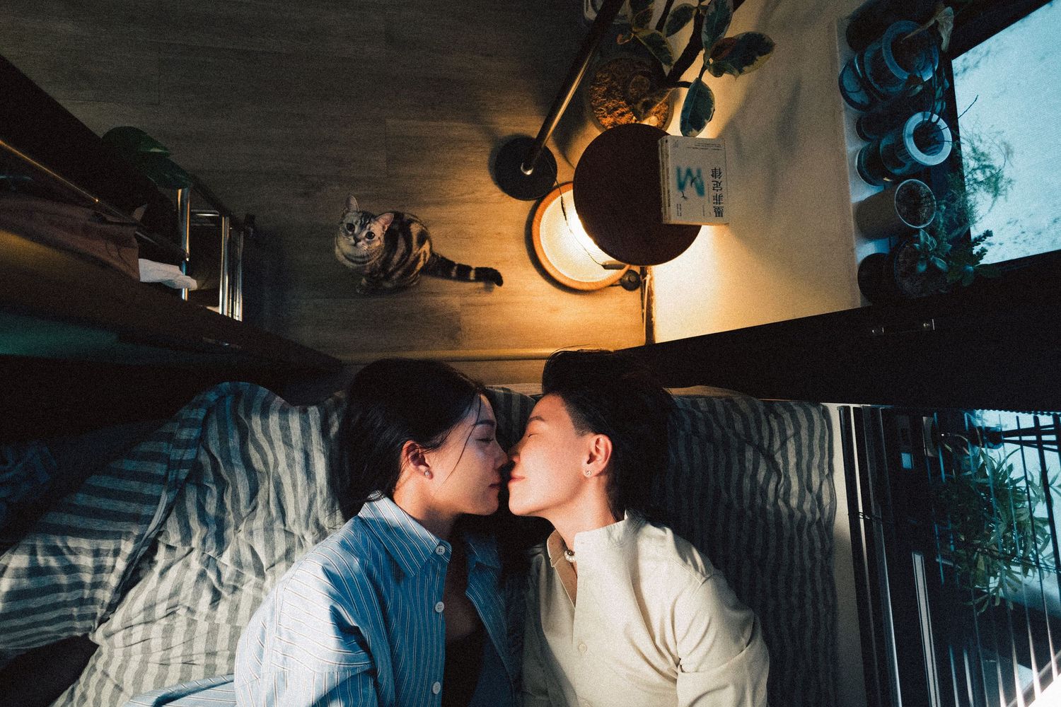 Young Asian couple sharing a kiss while lying in a cozy dimly lit bedroom.