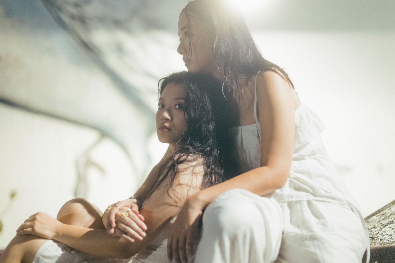 Two women in white dresses sitting together in a softly lit indoor setting.