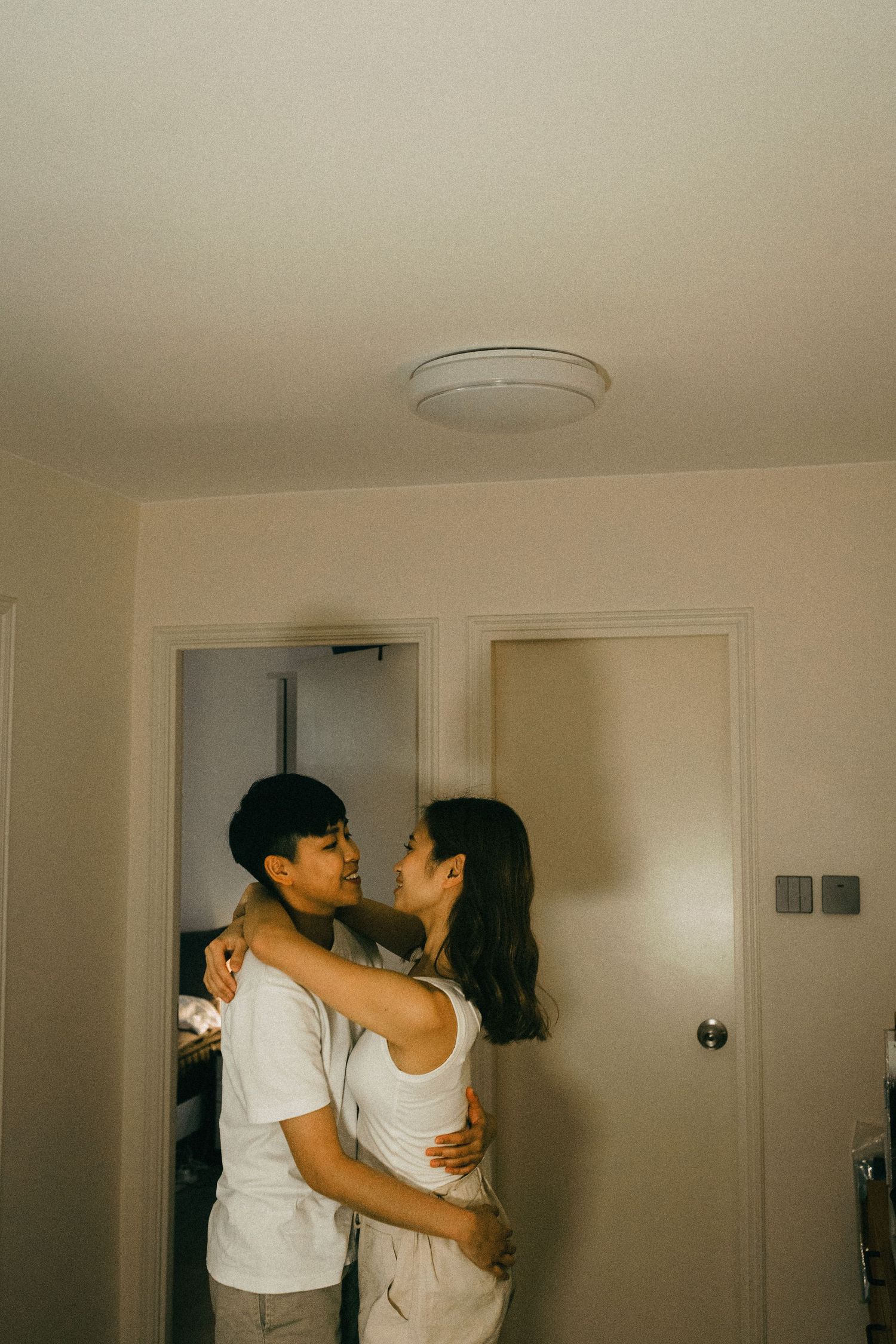A young Asian couple embracing and gazing at each other lovingly in a hallway.