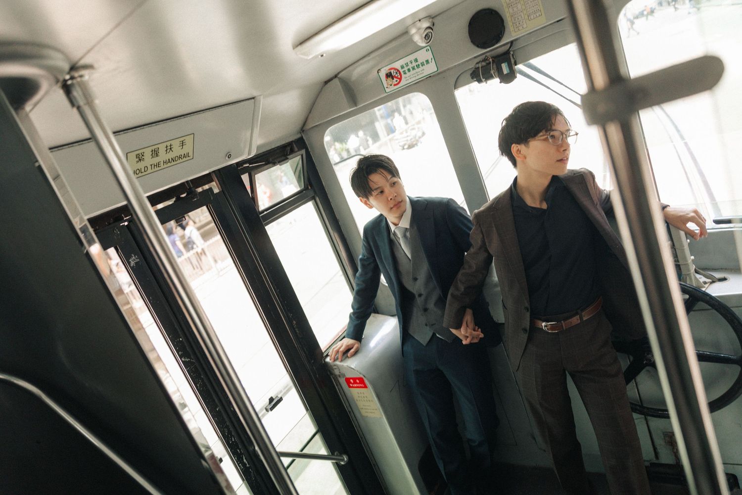 Two well-dressed Asian men standing near the doors inside a public tram in Hong Kong.