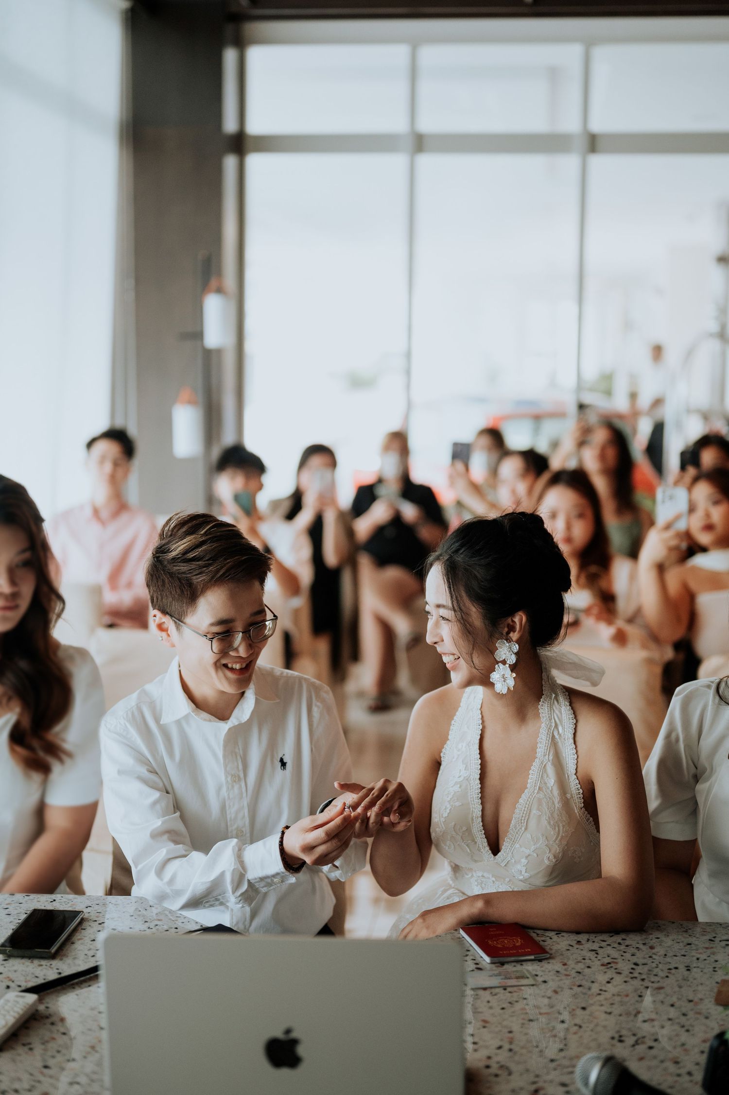 Couple exchanging rings at a wedding ceremony with smiling guests in the background.