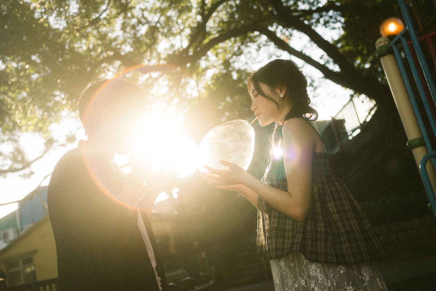 Two people holding a glowing bubble together in a sunlit park with lens flare and trees in the background.