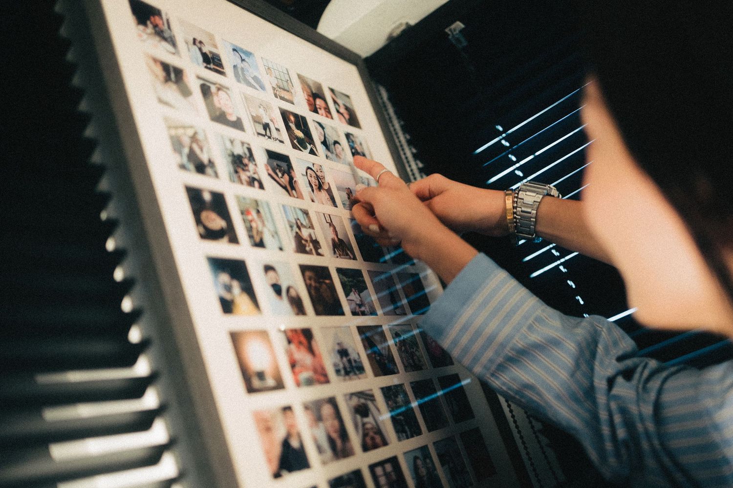 Person arranging a large grid of polaroid photos on a light board in dark room.