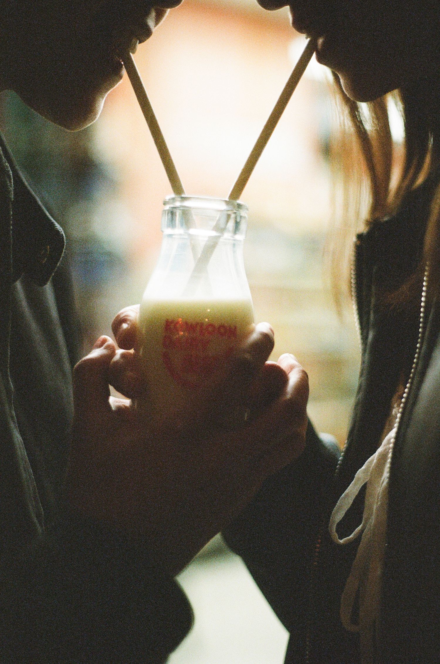 Couple sharing a milk drink with two straws from a Kowloon branded glass bottle.