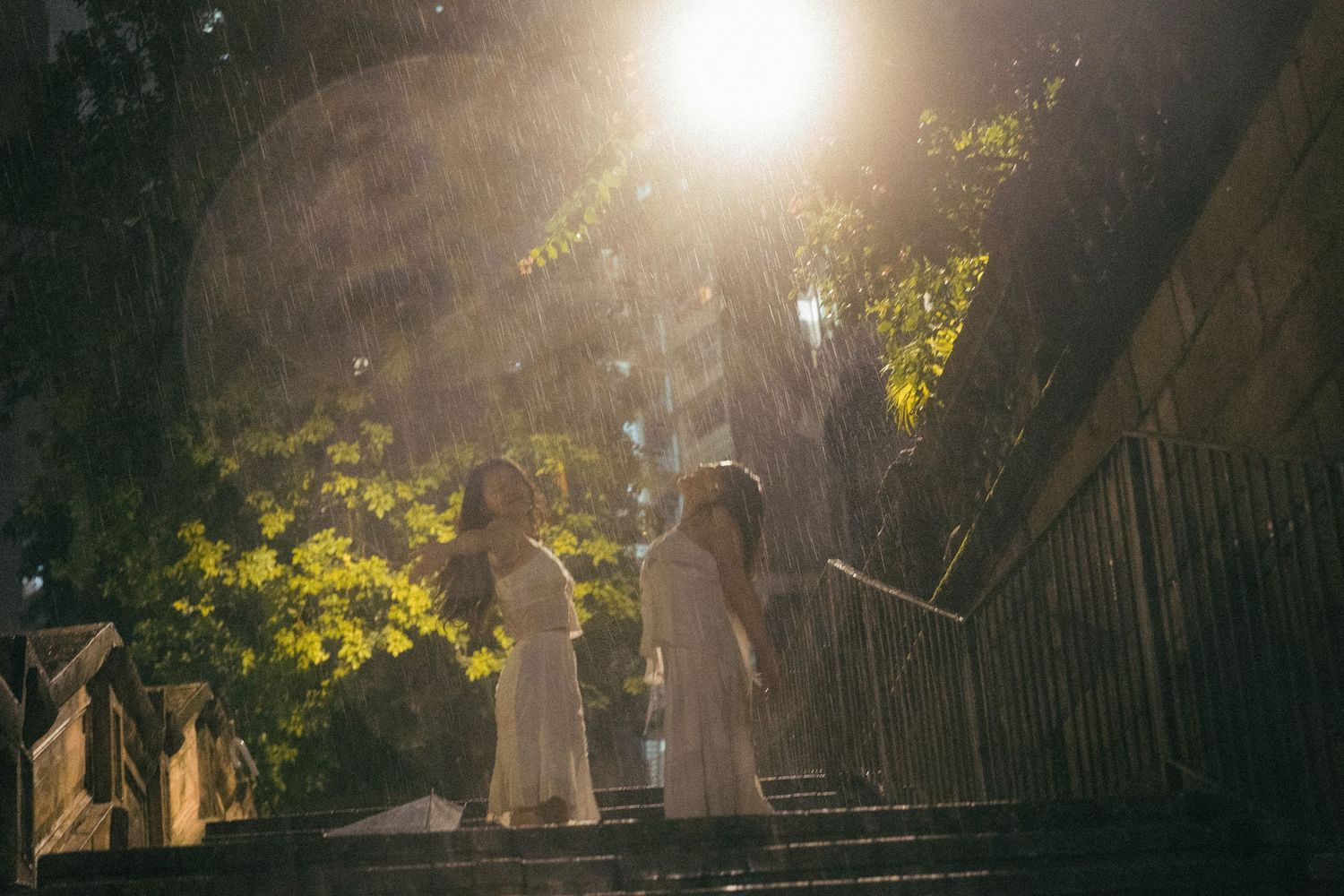 Two women in white dresses standing on steps in golden misty rain.