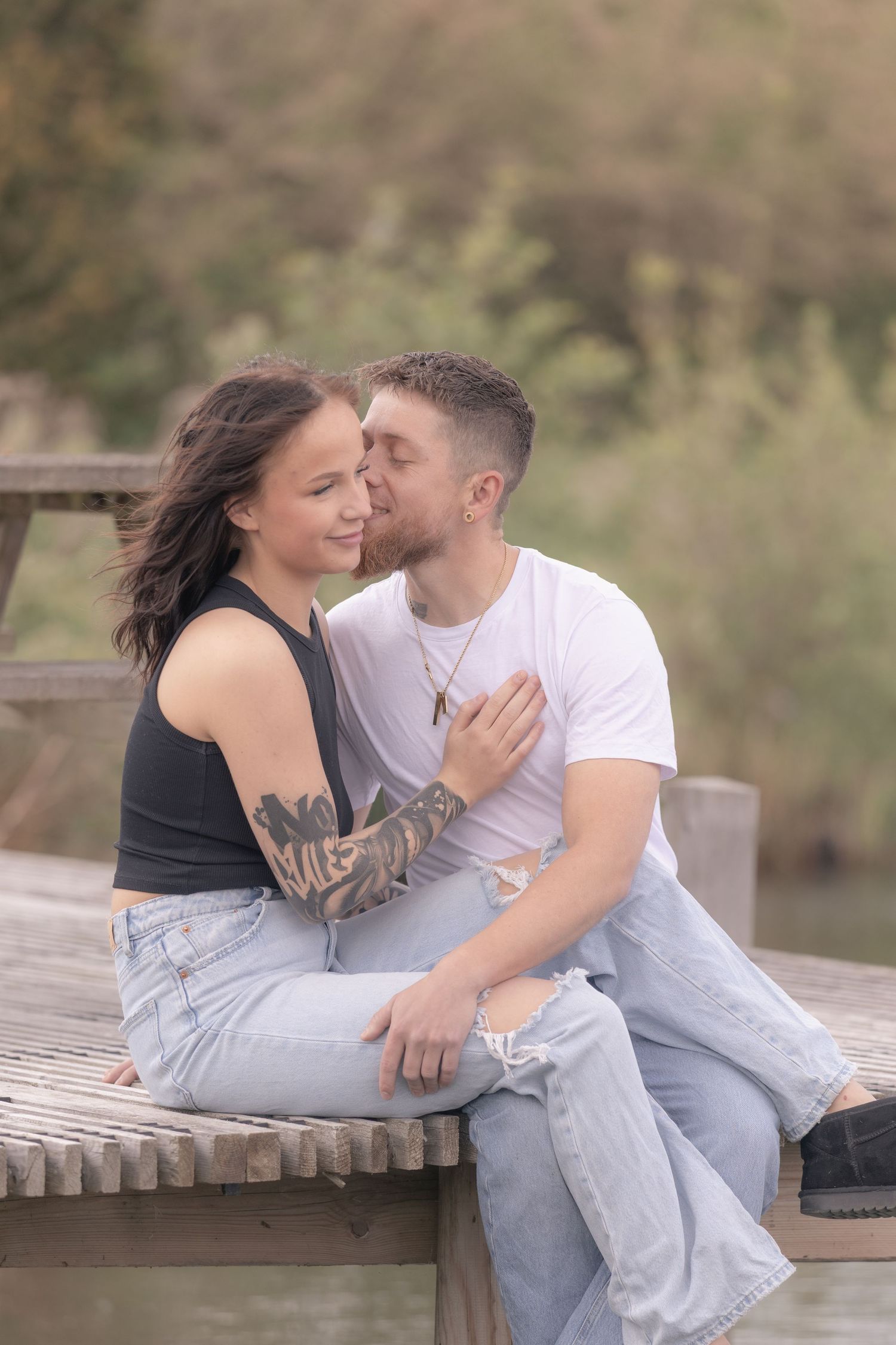 Couple sharing a tender kiss while sitting together on a wooden dock near a lake.