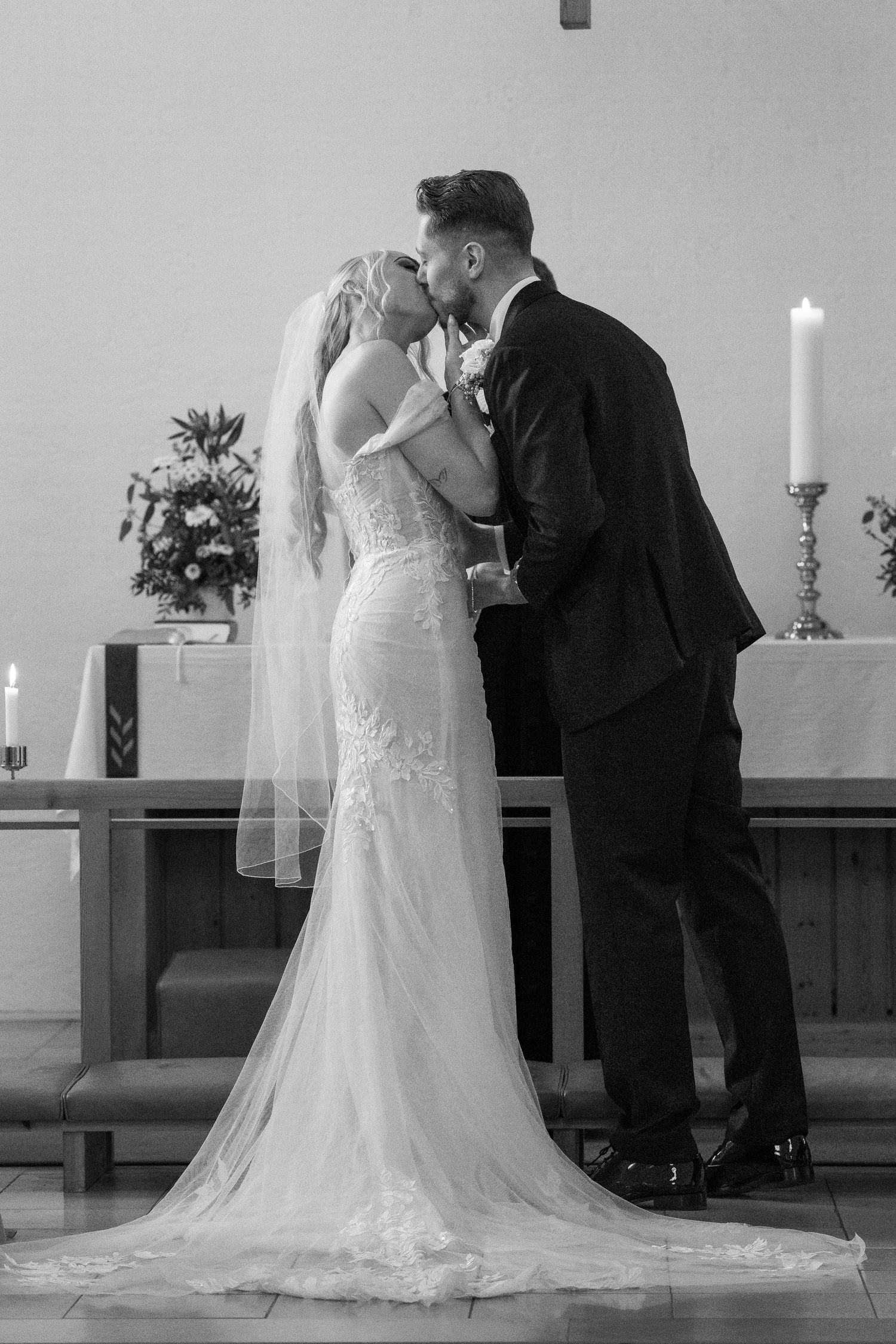 Bride and groom share first kiss at church altar in elegant black and white wedding photography.