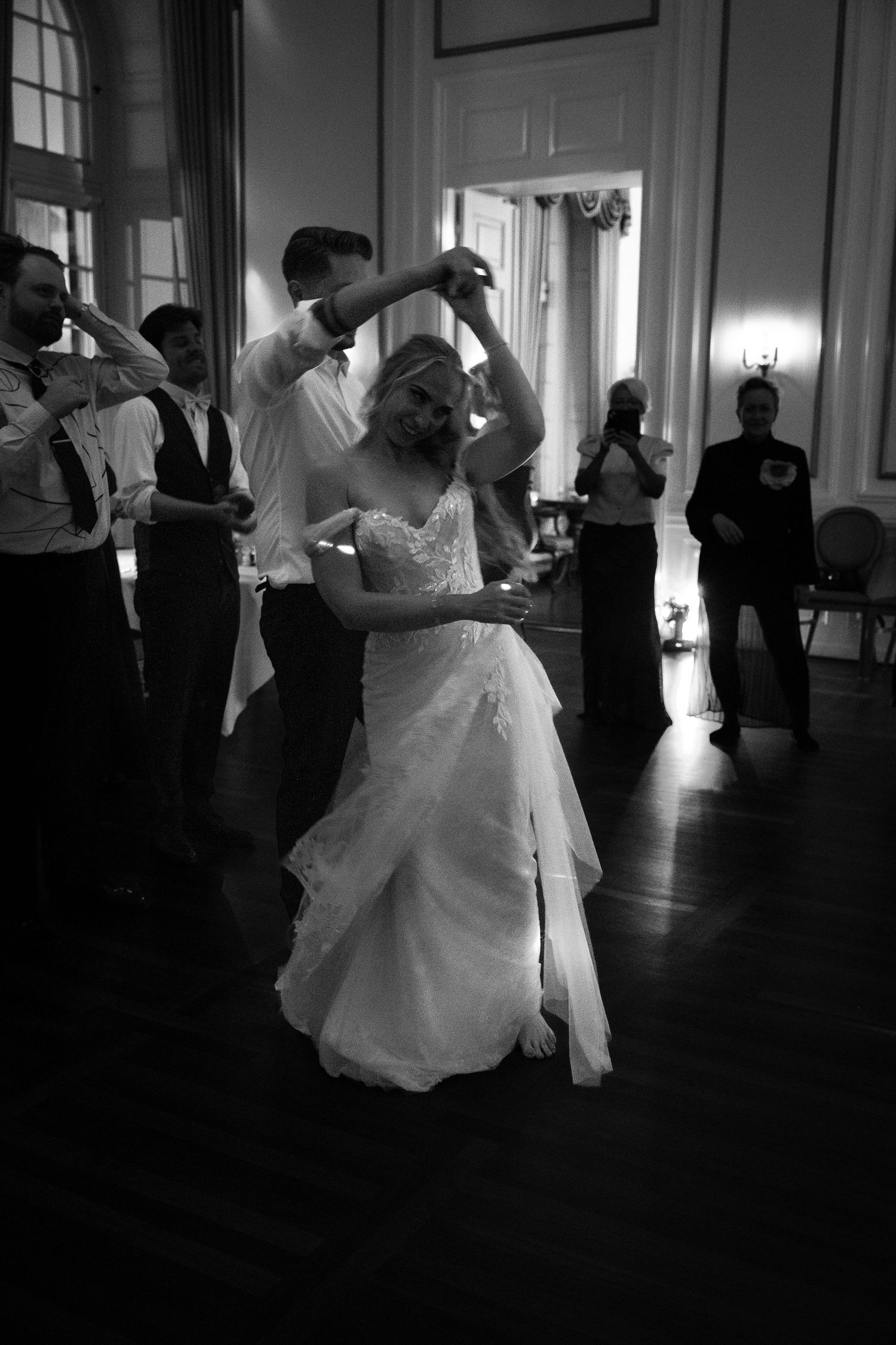Bride in a flowing white gown twirls during her first dance in an elegant black and white wedding ballroom.