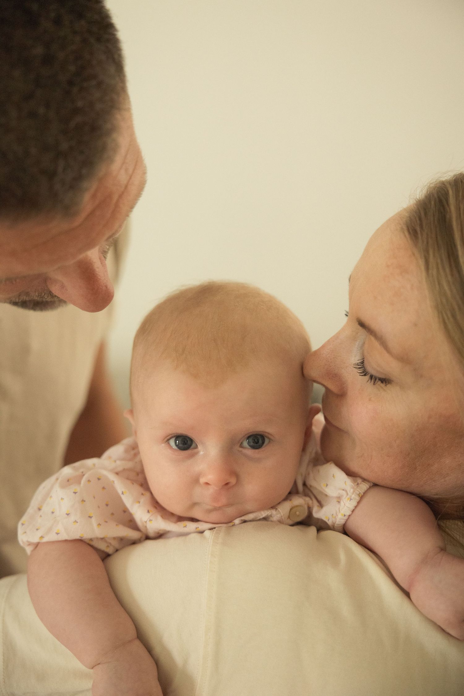 Parents lovingly kissing and holding their newborn baby with blue eyes in a tender family portrait.