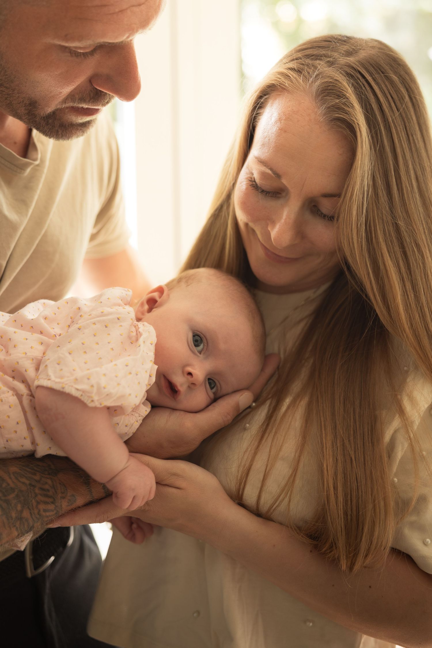 A loving couple smiles down at their newborn baby dressed in pink, sharing a tender family moment.