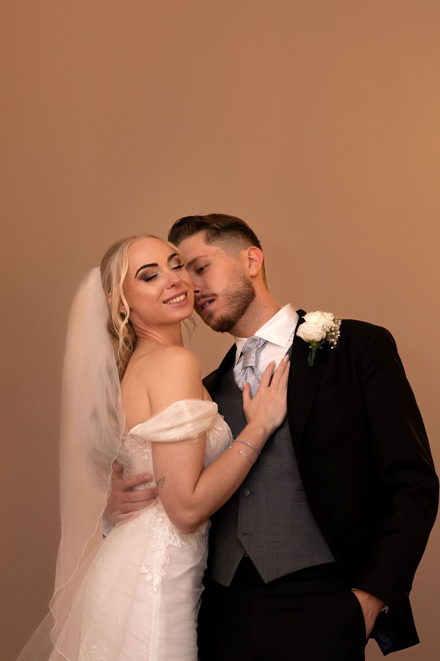 Bride and groom embrace tenderly in warm-toned studio portrait on their wedding day.