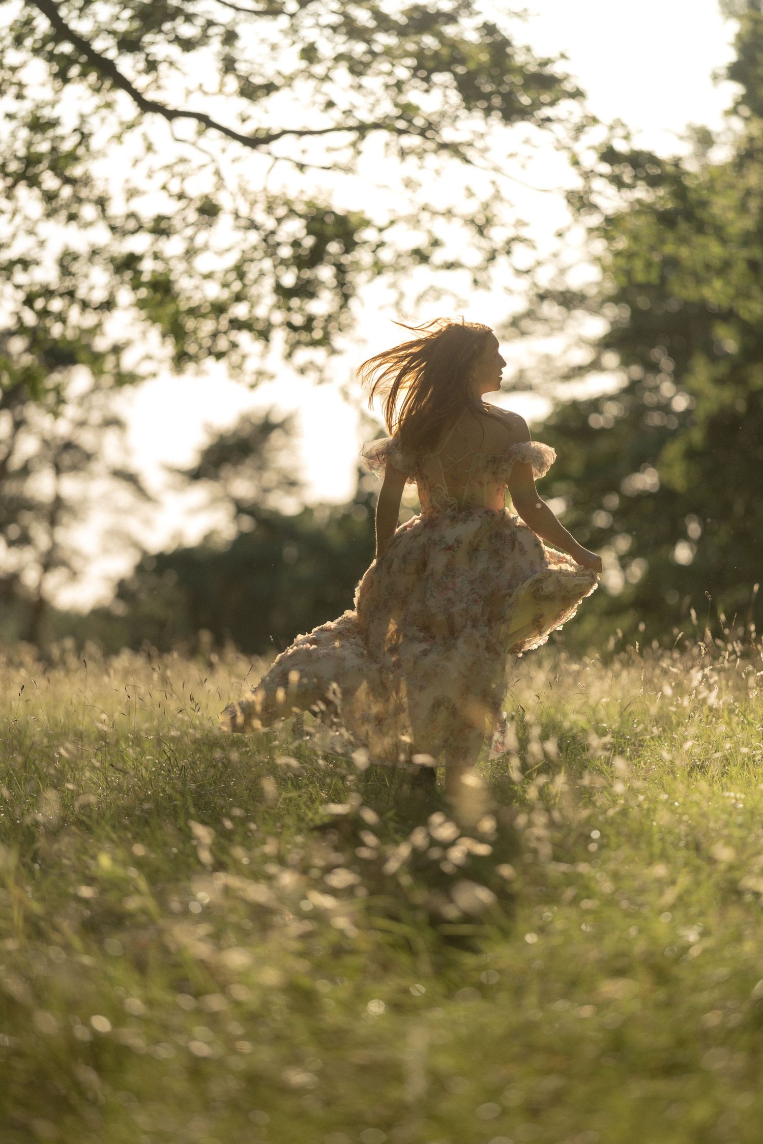 A woman in a floral dress runs through a sunlit meadow, her hair flowing as golden light filters through trees.