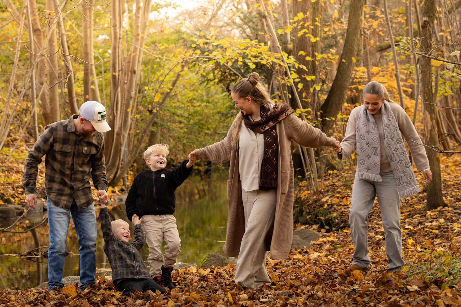 Family of five walking and holding hands through a golden autumn forest near a pond.