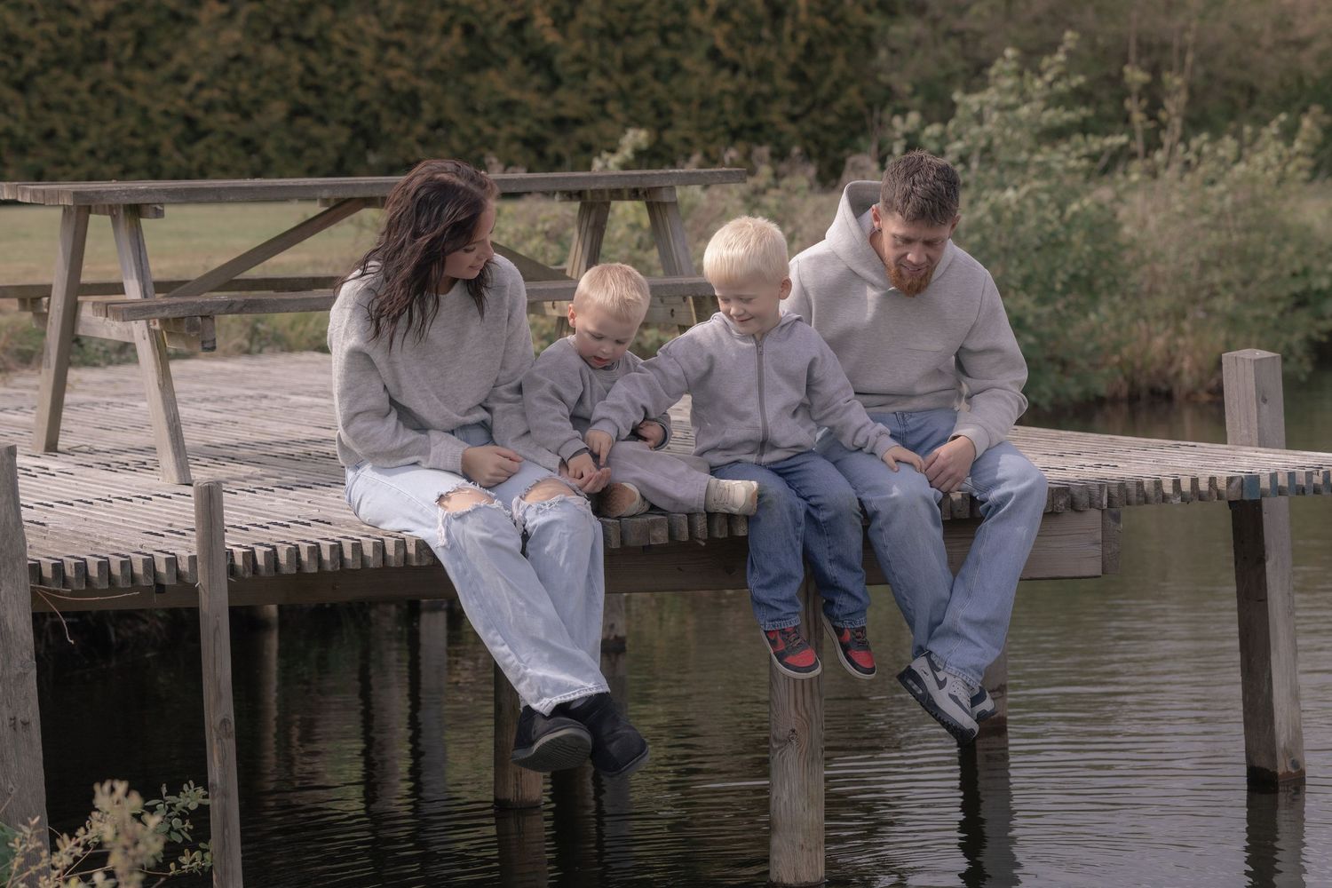 Family of four sitting together on a wooden dock over a calm lake on an overcast day.