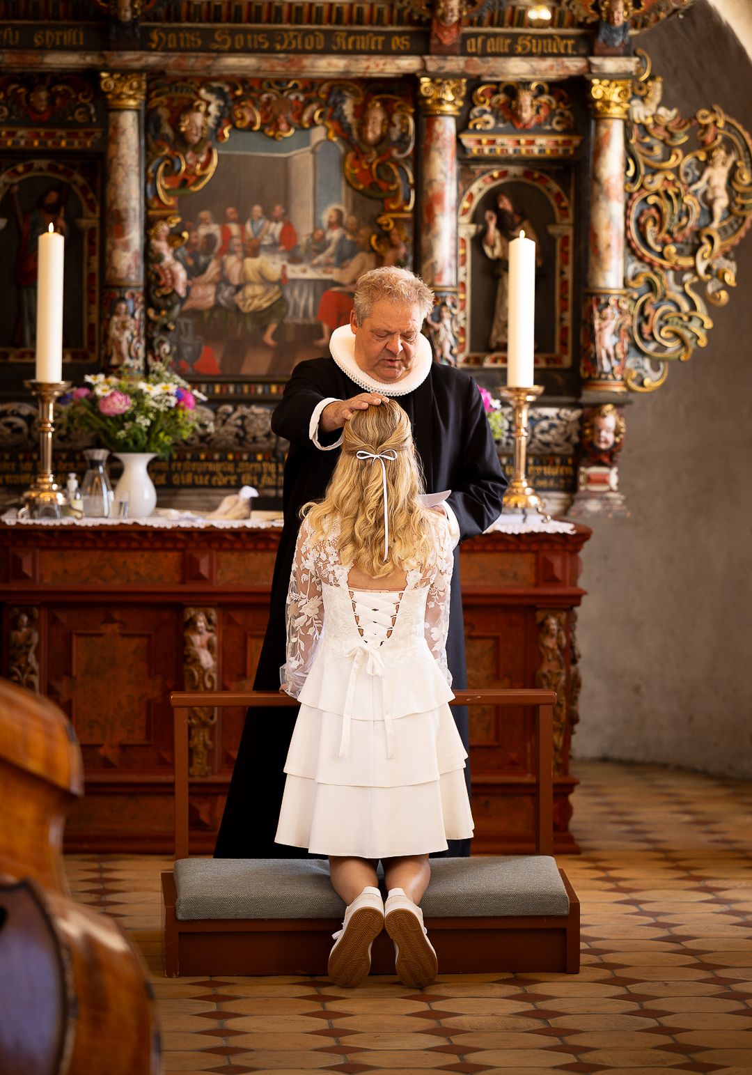Pastor placing hands on confirmand girl kneeling at ornate wooden church altar.