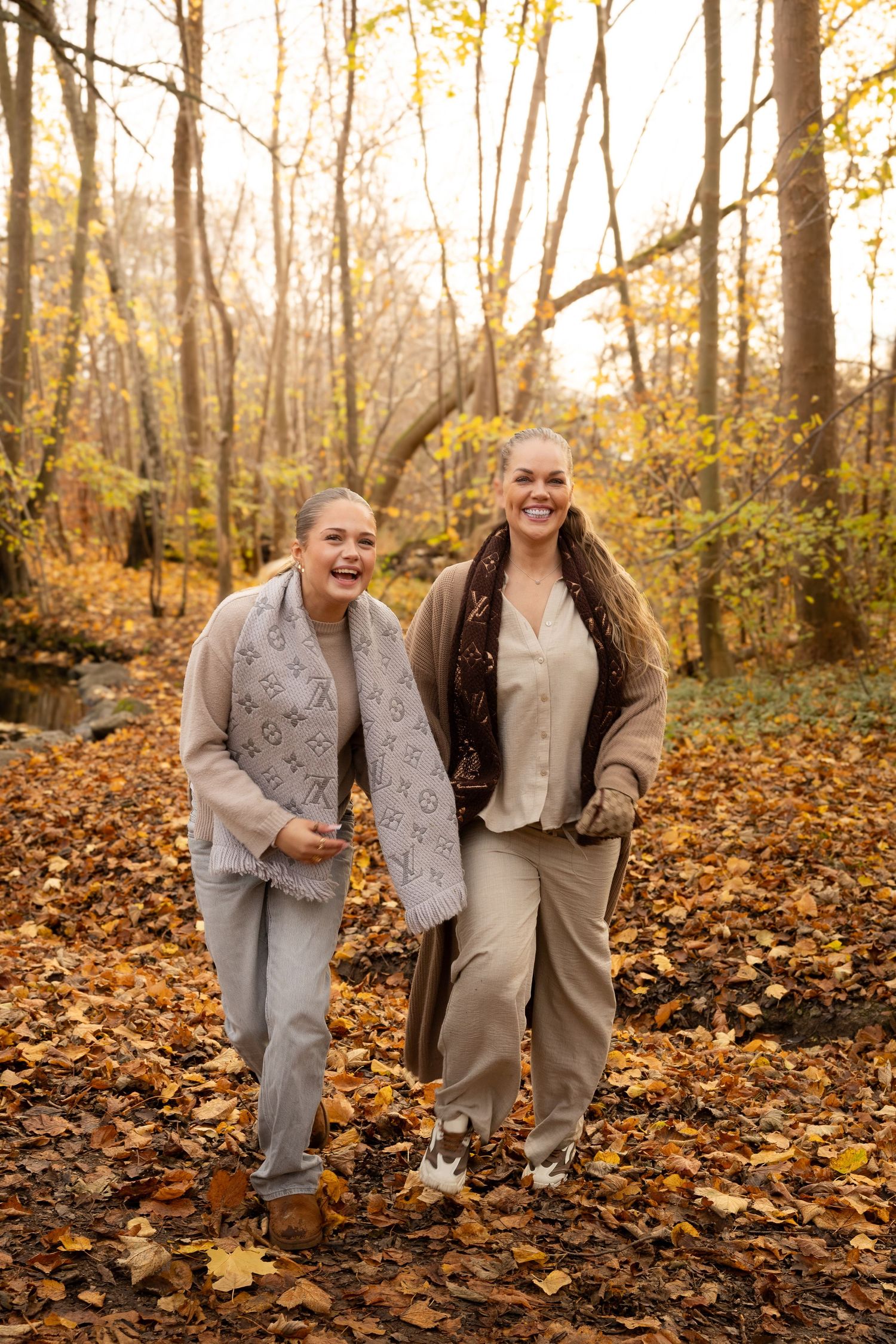 Two women laughing and walking together in a colorful autumn forest.
