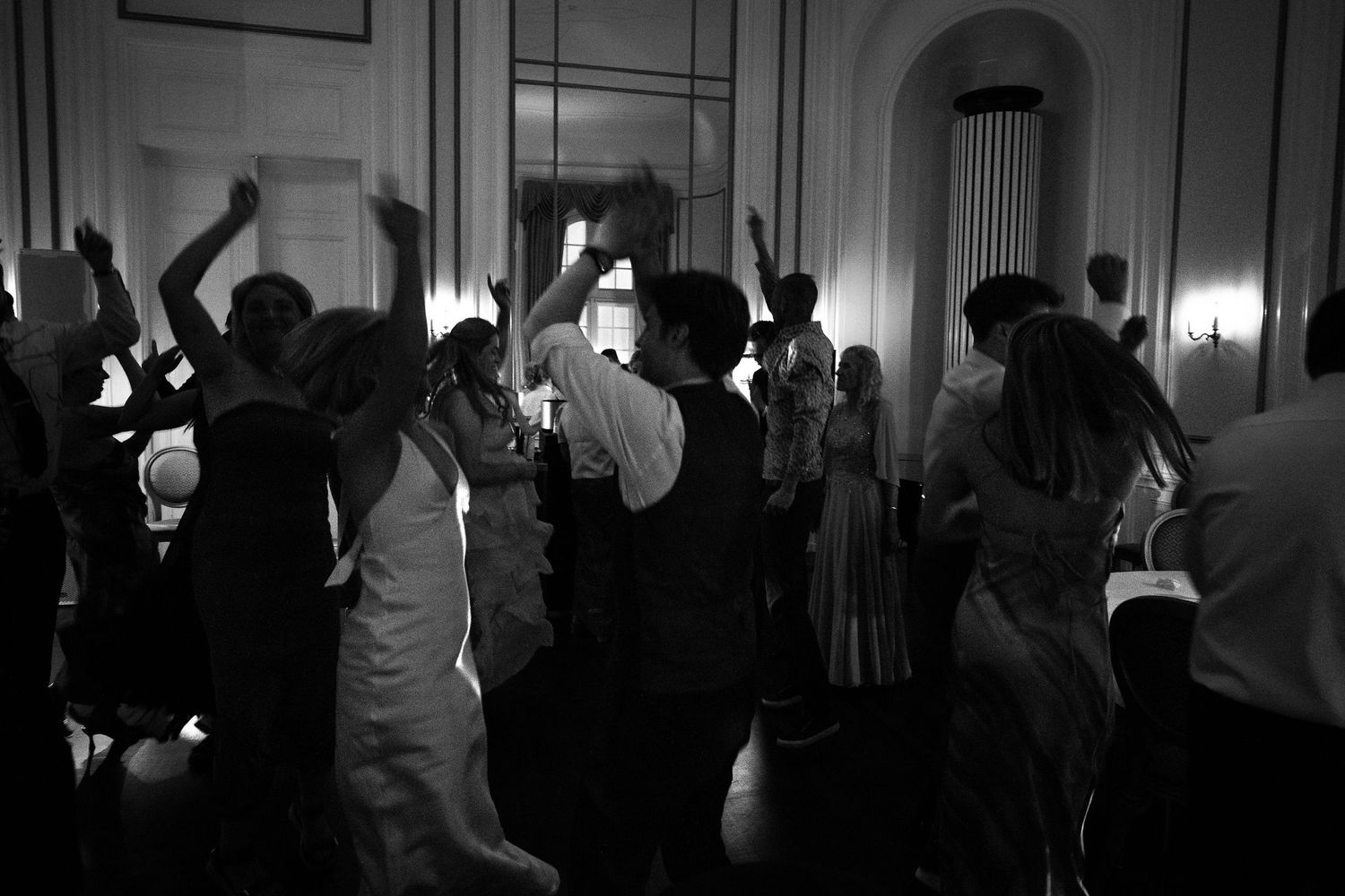Wedding guests fill the dance floor in a grand ballroom captured in a lively black and white reception photo.