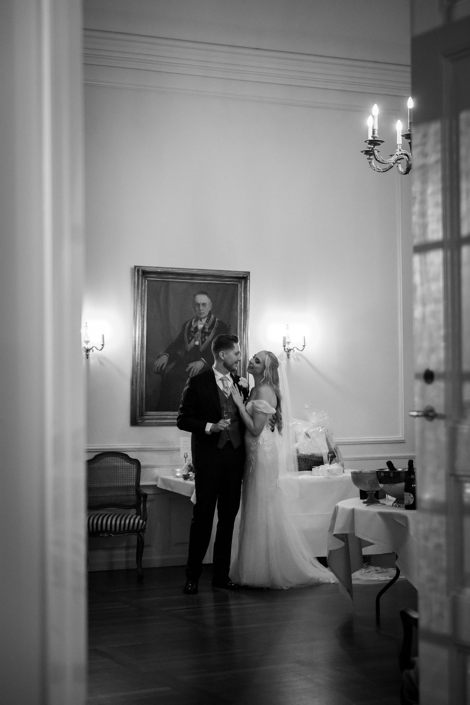 Bride and groom share an intimate moment in an elegant black and white wedding reception hall with portrait and chandelier.