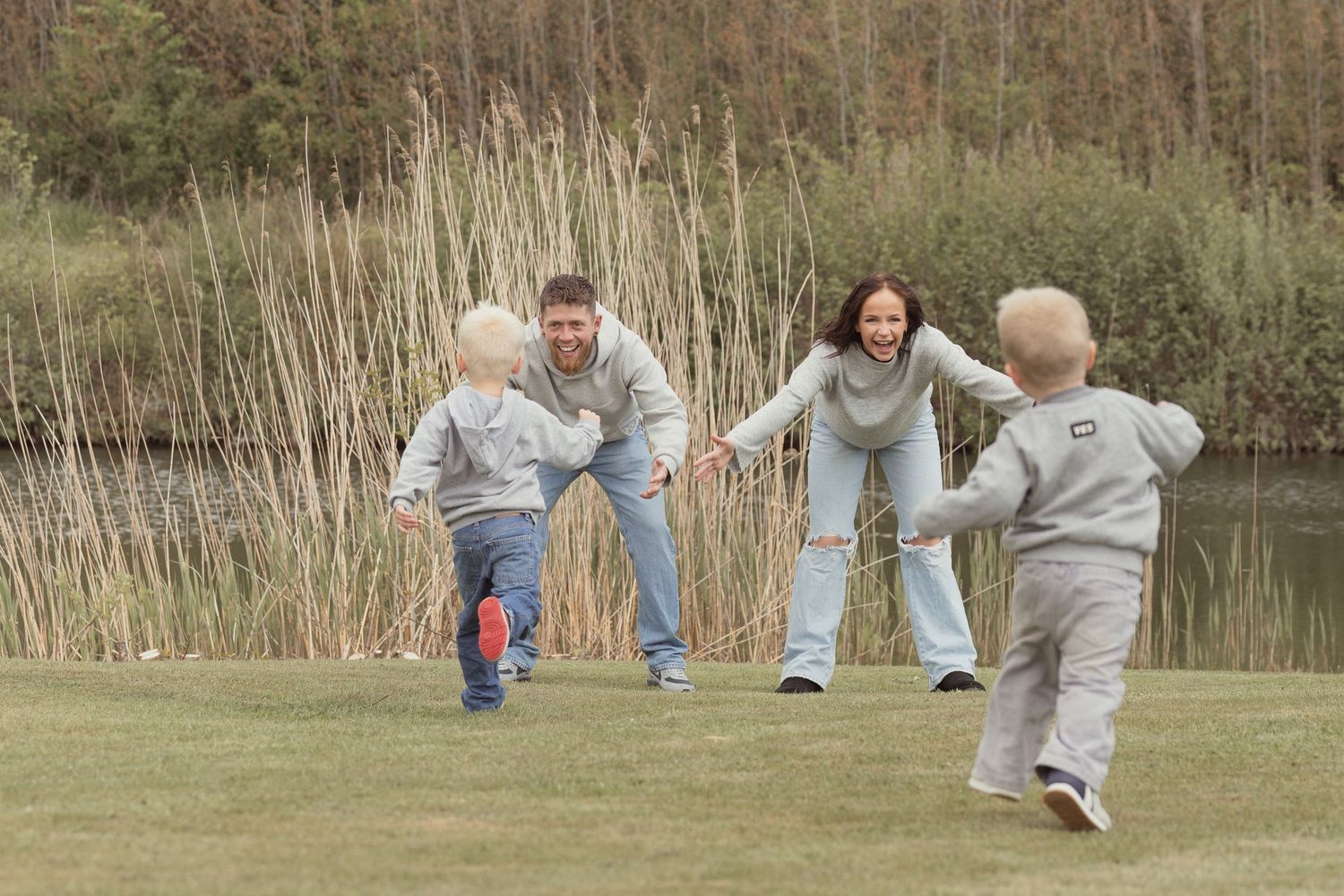 Happy family with two young children running toward parents with open arms in park.