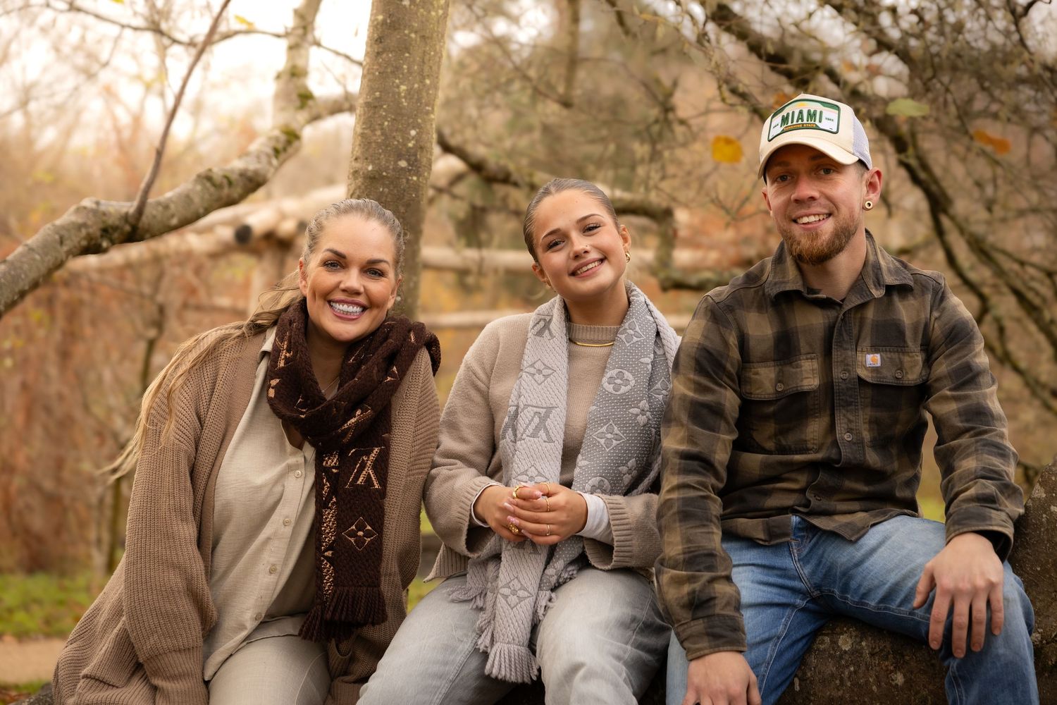 Three adults smiling and sitting together outdoors in a park during autumn season.