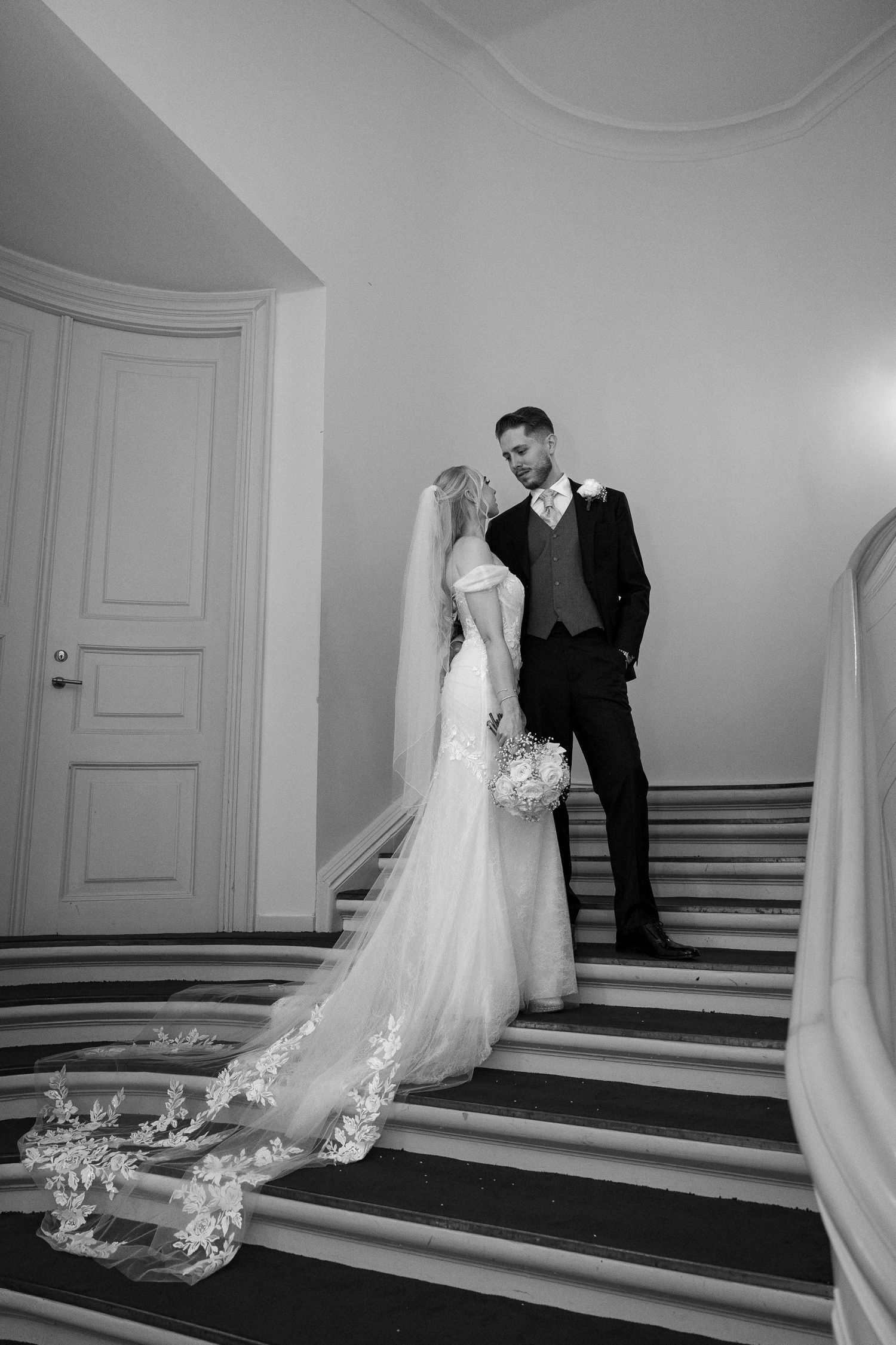 Bride and groom sharing intimate moment on elegant marble staircase in black and white.