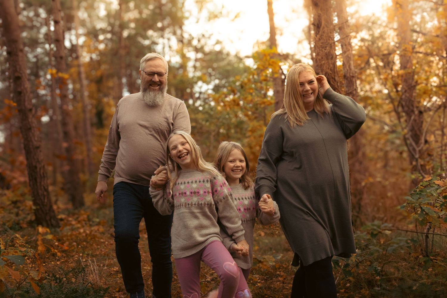 Grandparents walking with two granddaughters in a sunny autumn forest.