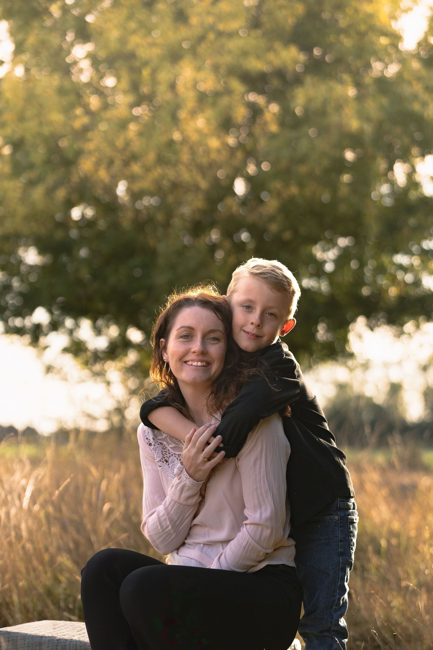 Loving mother and son hugging outdoors in autumn park with warm golden sunlight background.