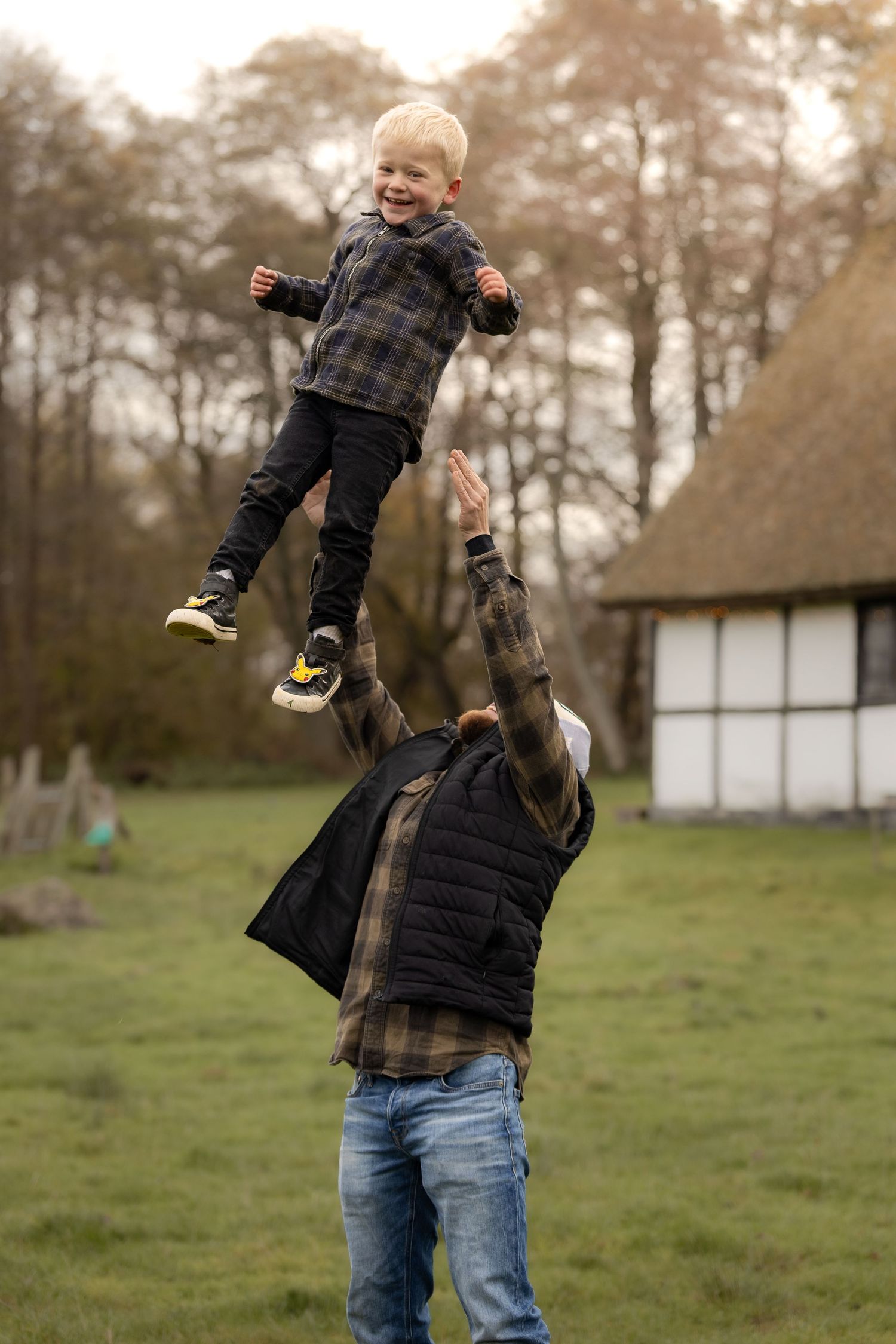 Father joyfully tossing his laughing young son high in the air in a green outdoor setting.
