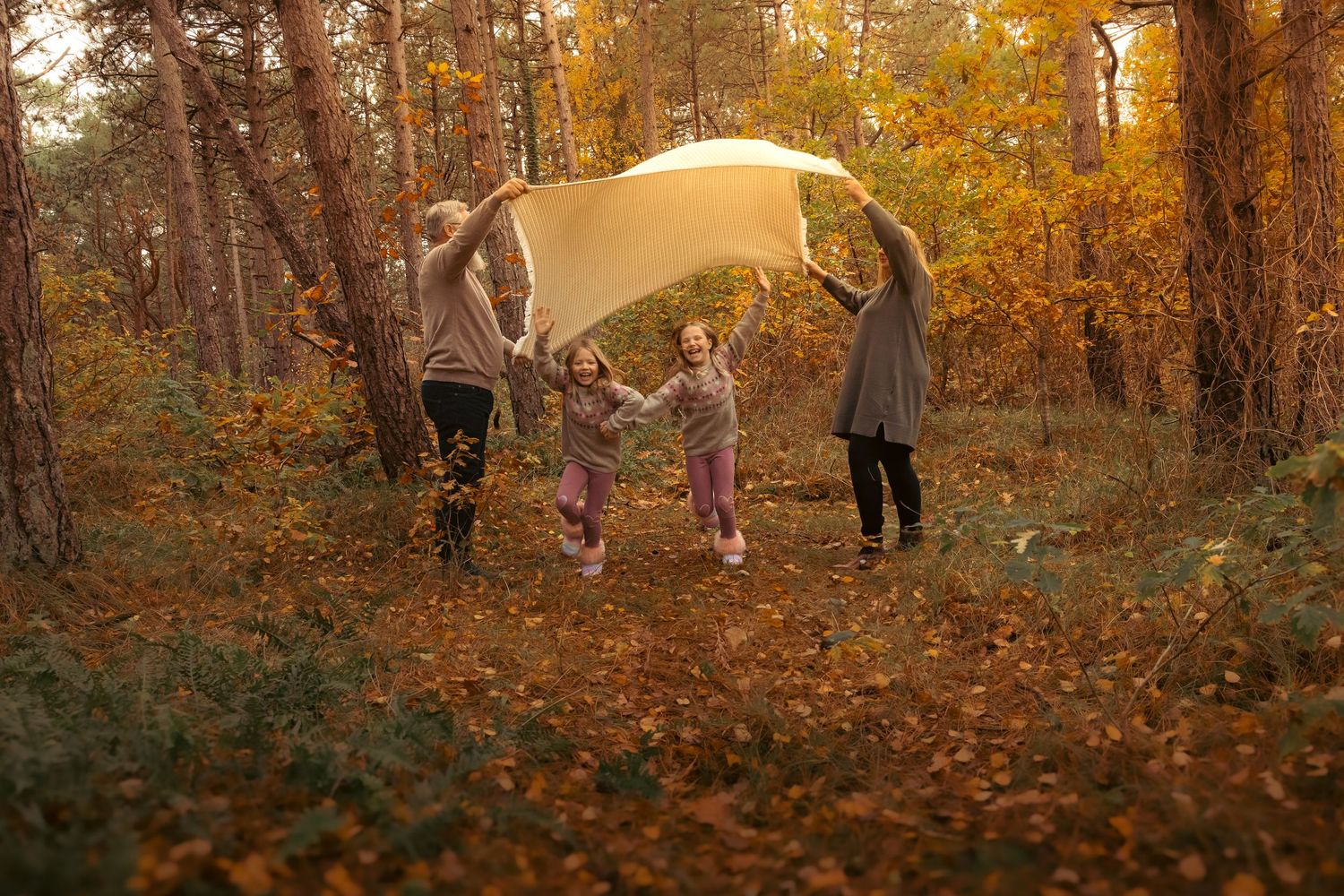 Family playing under a yellow blanket in an autumn forest with golden leaves.
