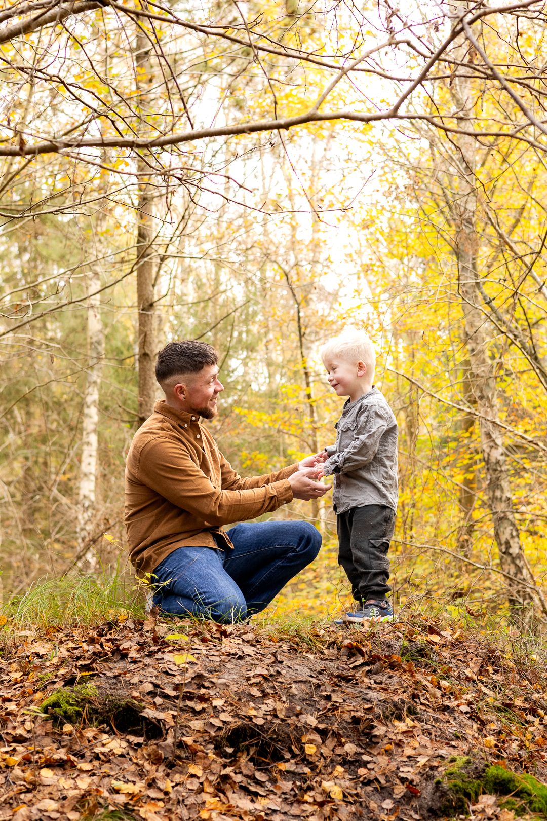 Father kneeling to interact with smiling toddler son in colorful autumn woodland.