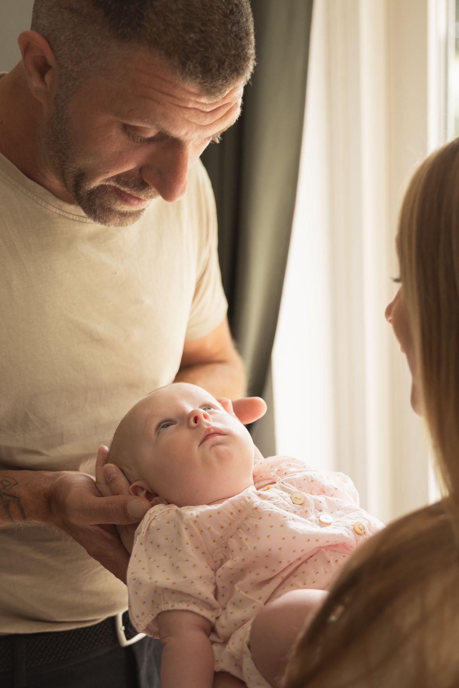 Parents lovingly gazing at their newborn baby near a sunlit window indoors.