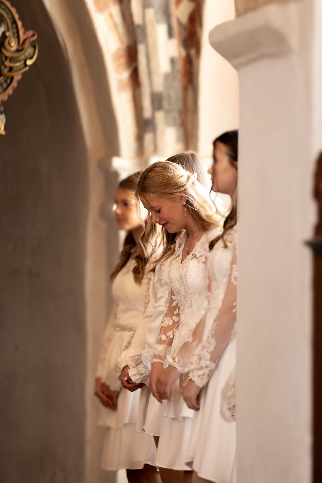 Girls in white lace dresses standing in a church aisle during a confirmation ceremony.