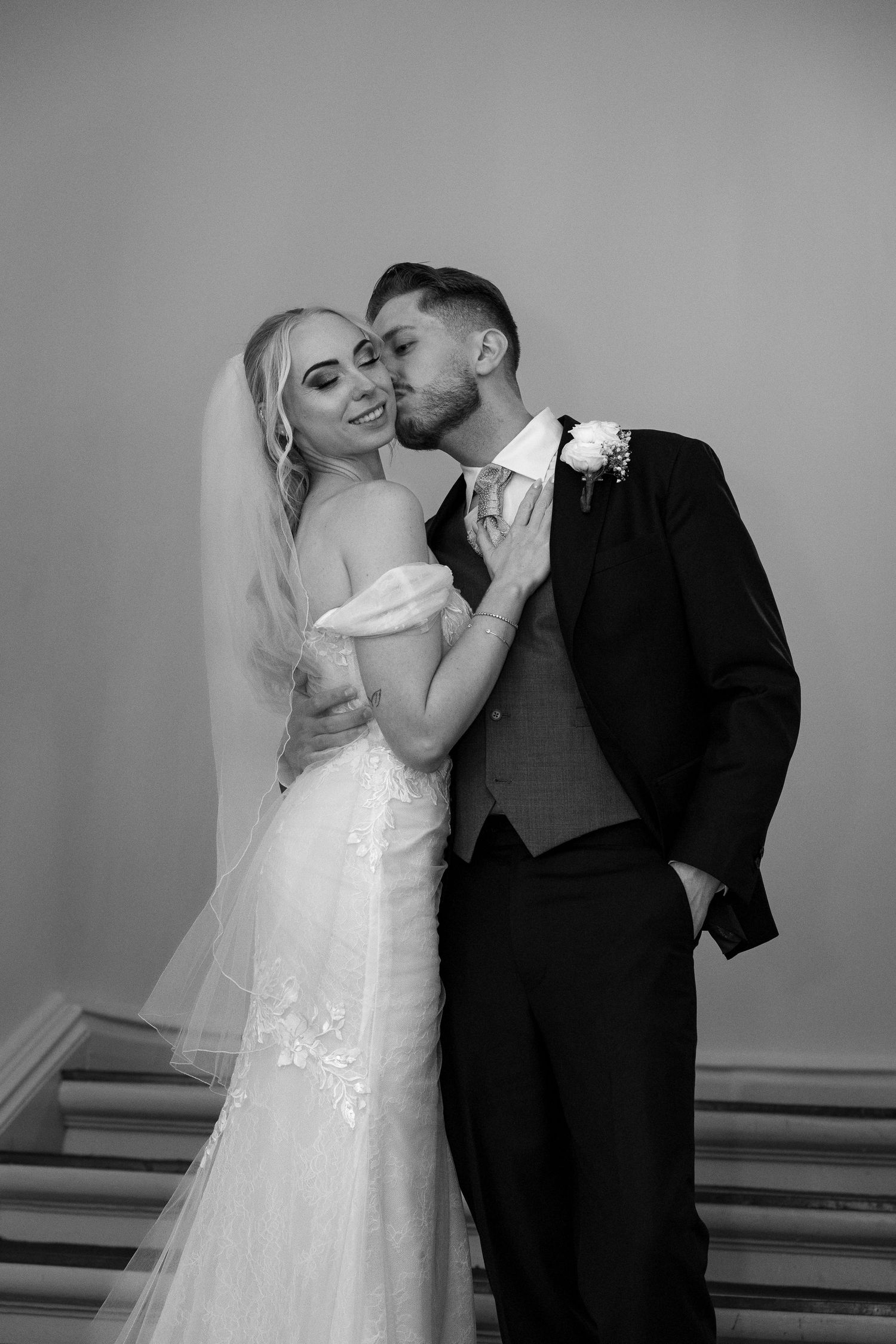 Groom kissing bride on cheek in romantic black and white wedding portrait.