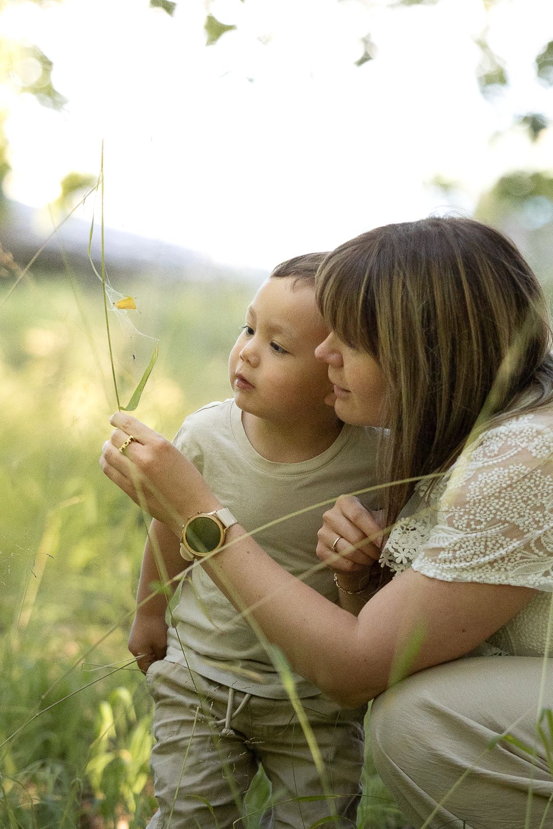 Mother and young son examining a wildflower together in a sunny meadow.