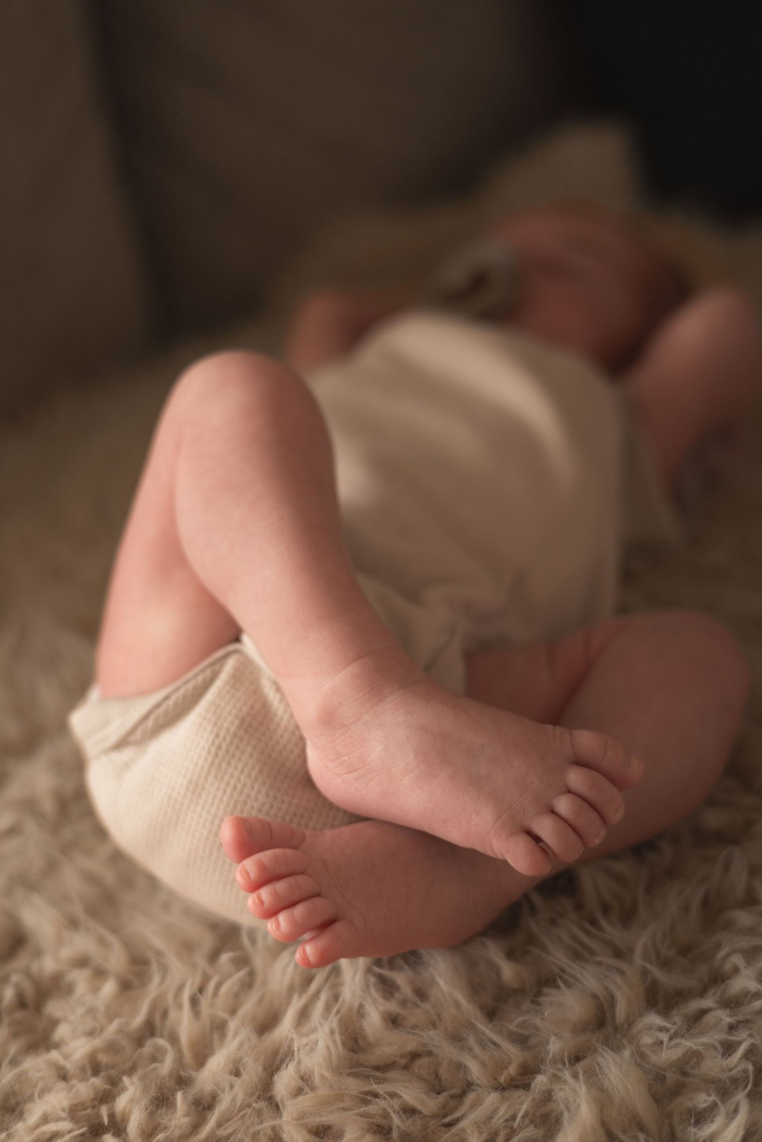 Close-up of a newborn baby's tiny feet and legs resting on a soft fluffy cream blanket.