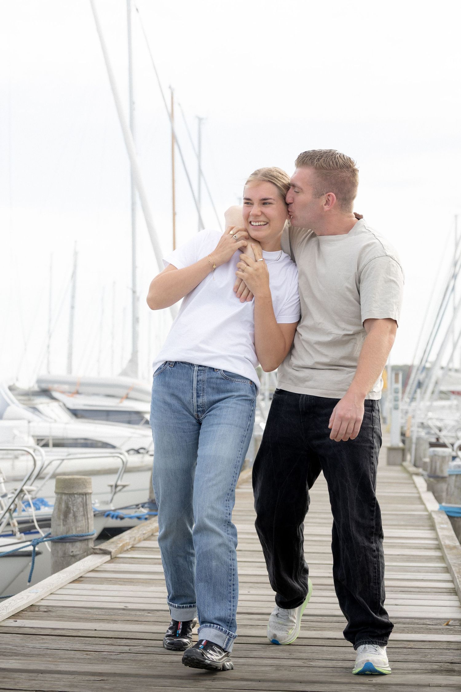 Man whispering in laughing womans ear while walking together along a sunny marina dock.