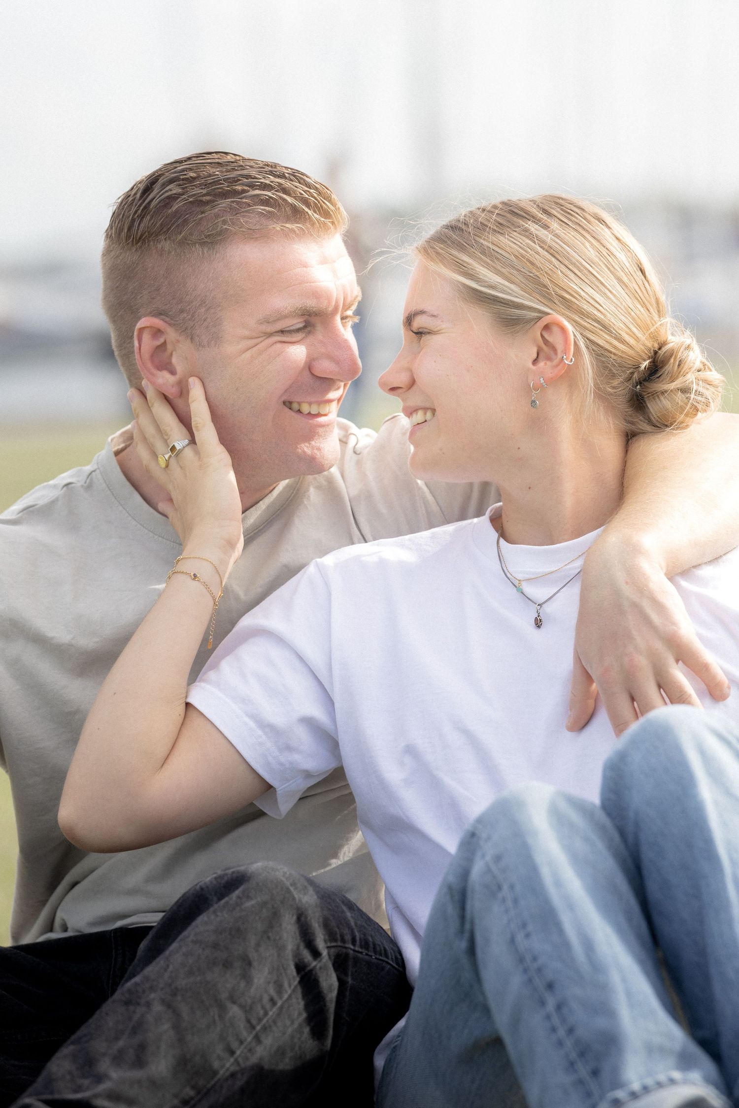 Happy couple sitting outdoors, smiling at each other, woman gently touching mans face.