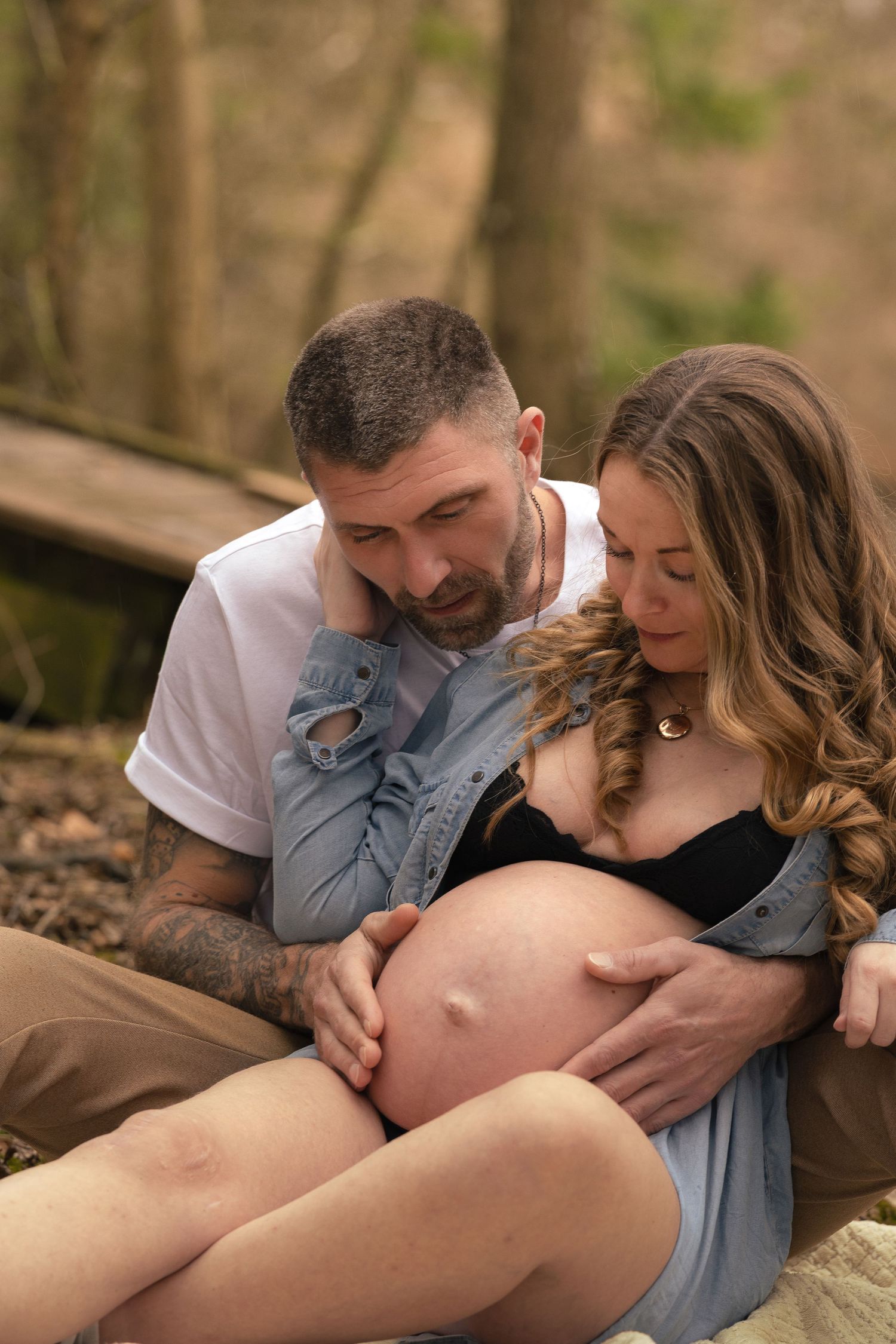 A couple shares a tender moment outdoors, with the man gently touching the pregnant woman's bare belly.