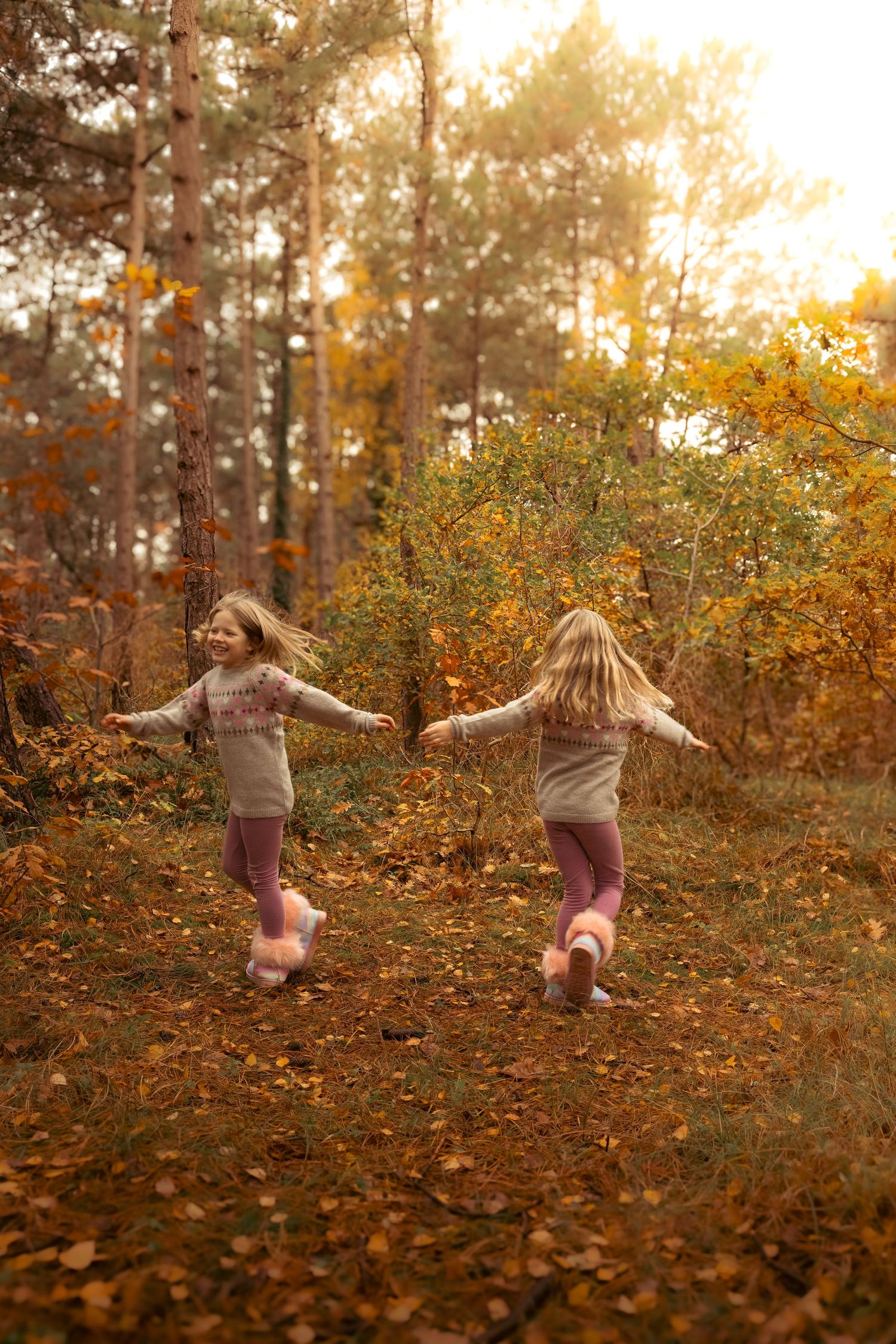 Two young girls running and holding hands in a golden autumn forest.