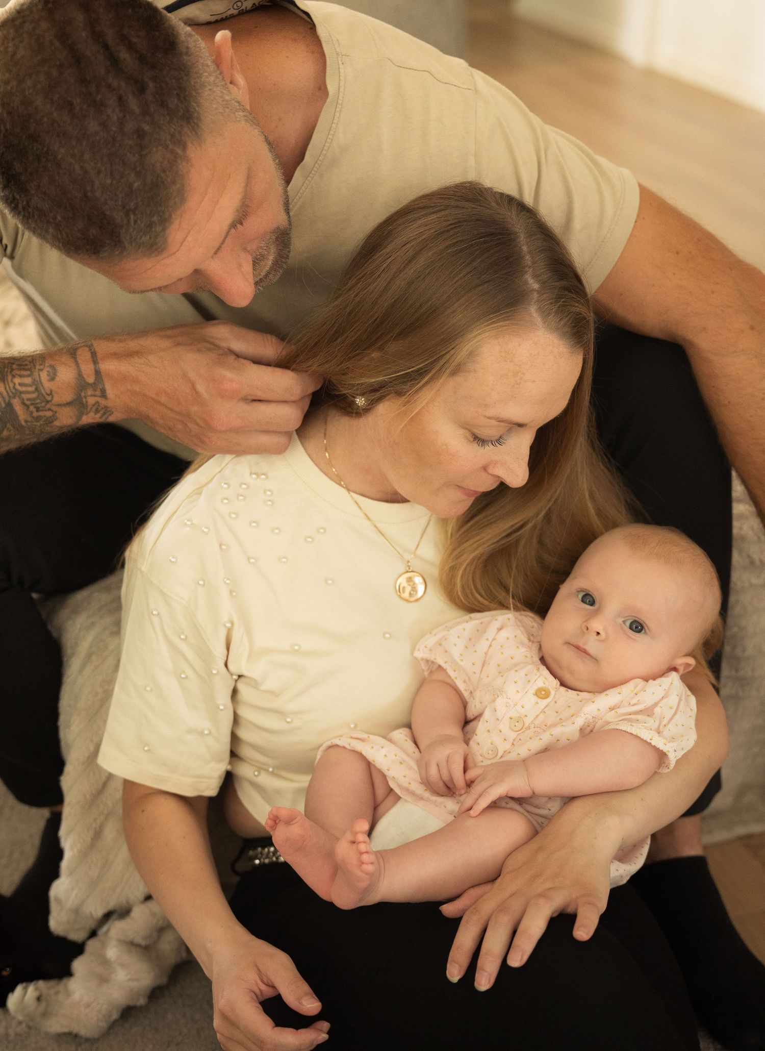 A tattooed father kisses his wife's head as she holds their newborn baby in a tender family portrait.
