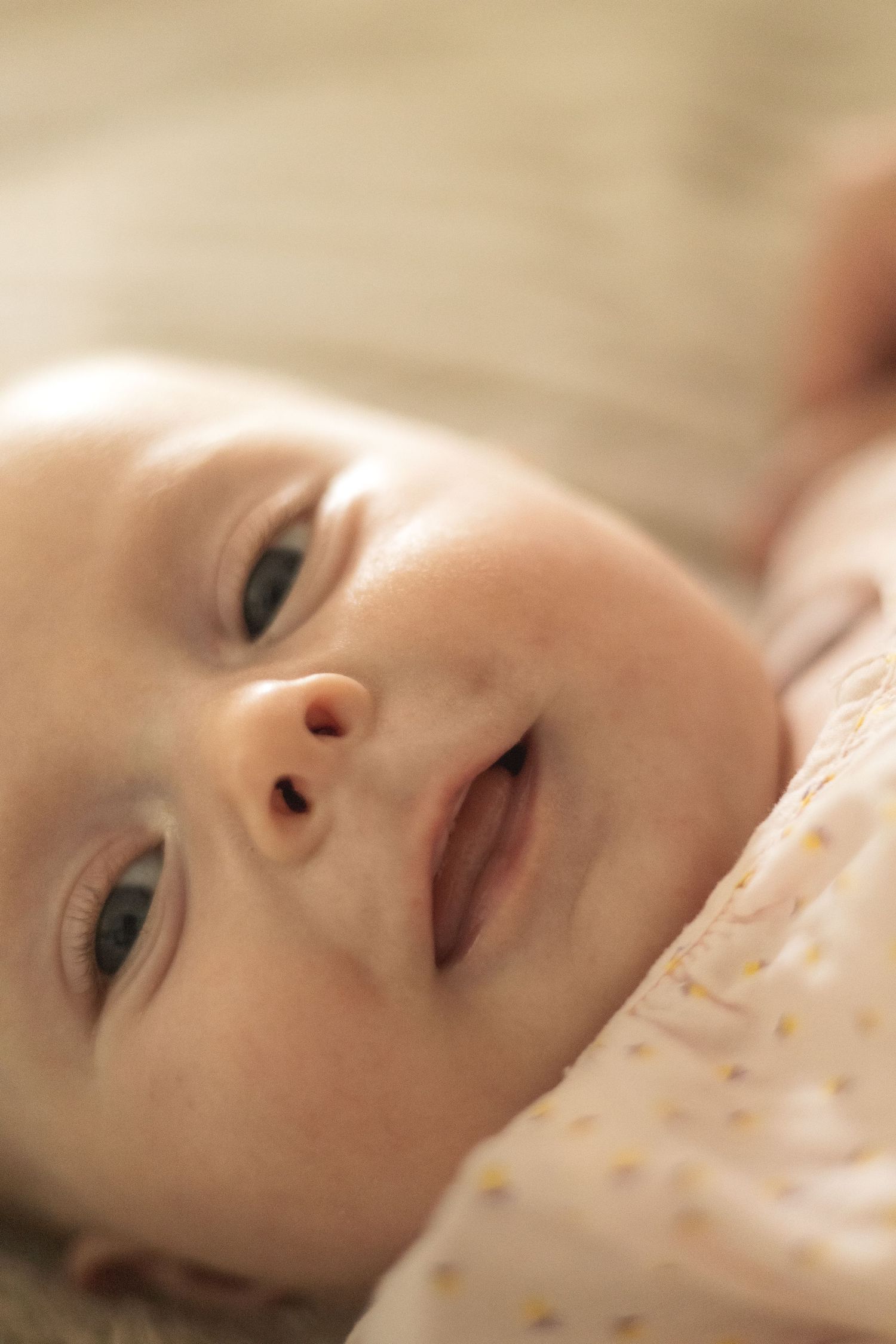 Close-up portrait of a smiling baby lying on their back, looking up with bright eyes and rosy cheeks.