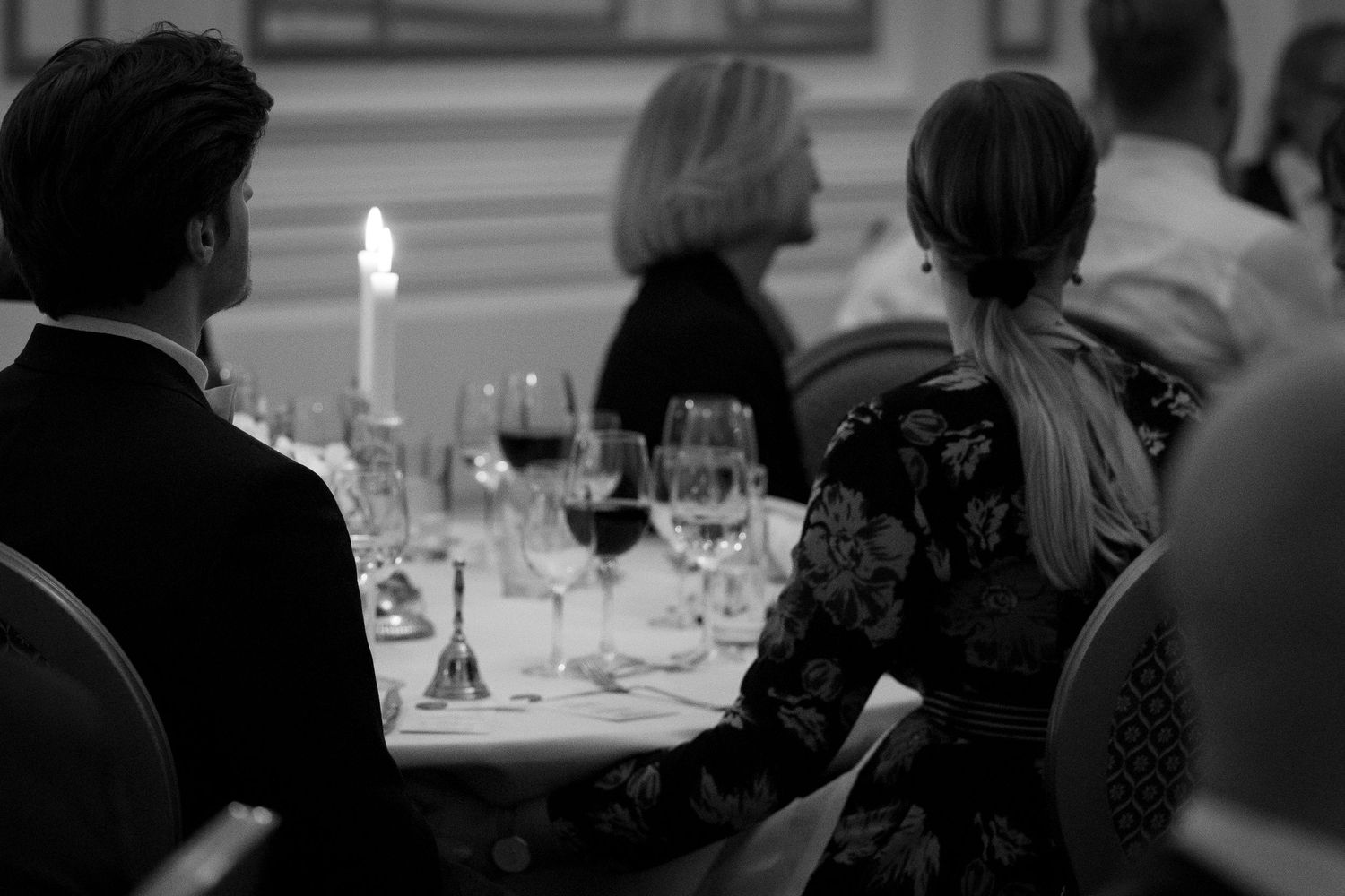 Wedding guests seated at a candlelit dinner table with wine glasses in a black and white reception photo.