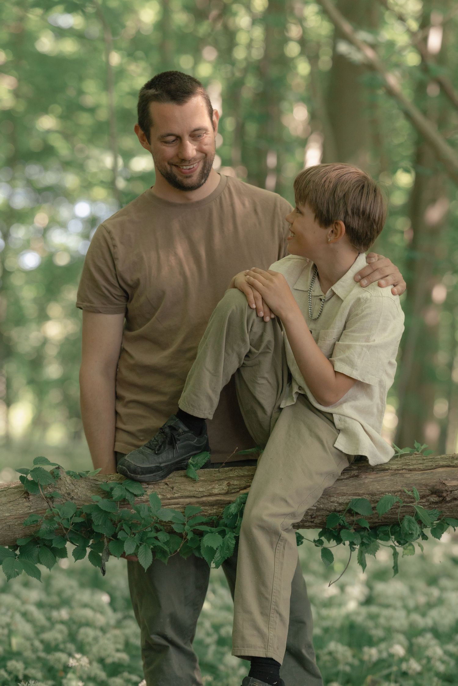 Father and son sharing a joyful moment on a fallen log in green woods.