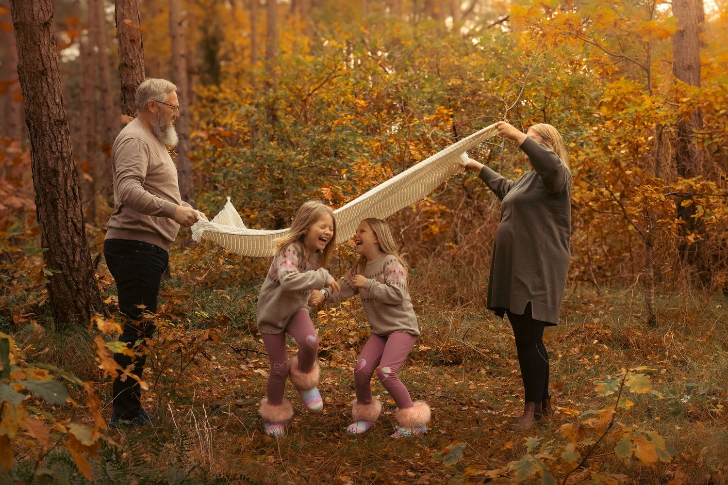Two adults and two young girls play with a white blanket in a colorful autumn forest.