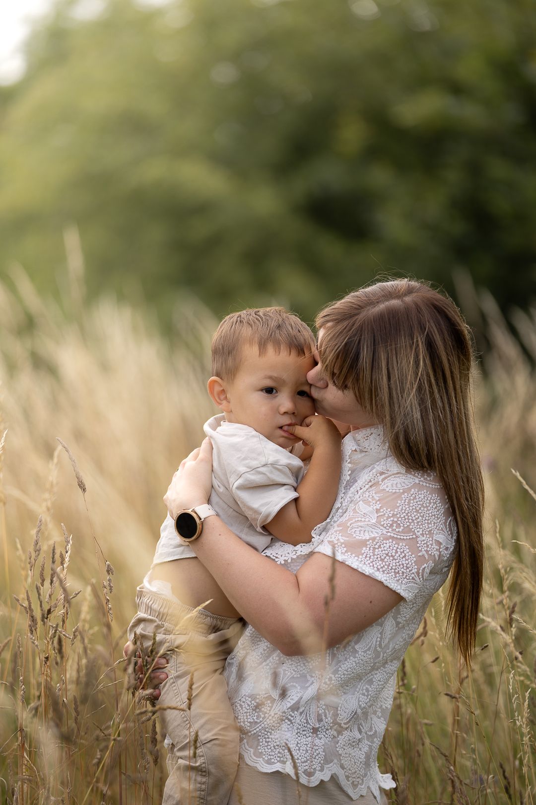 A mother tenderly holds her toddler son in a golden wheat field, touching foreheads in a warm embrace outdoors.