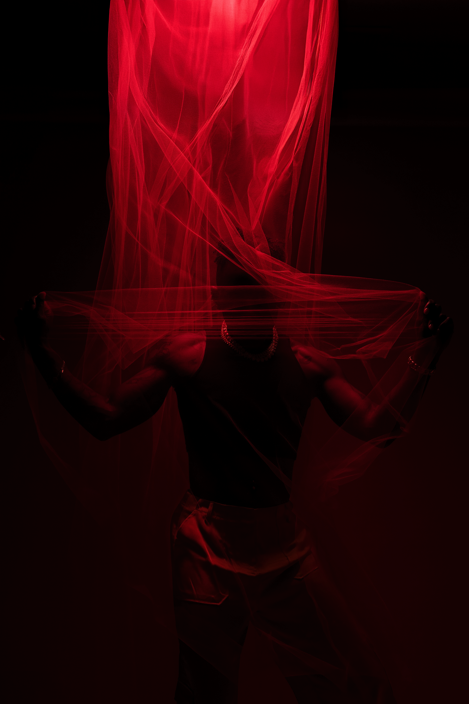 Dramatic silhouette of a person holding flowing red sheer fabric illuminated by red light against black background.